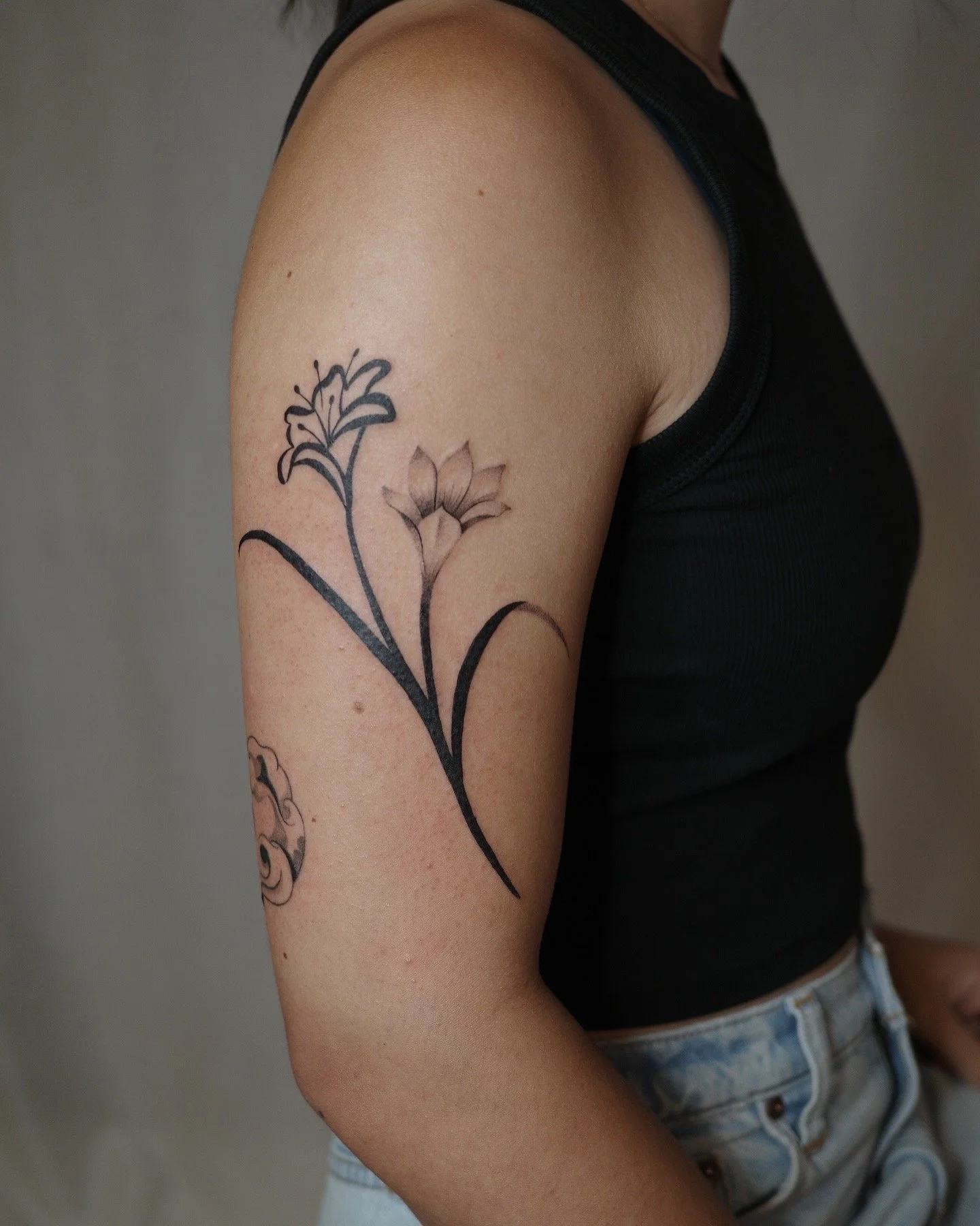 A person's upper arm with a floral tattoo, wearing a black sleeveless top and denim shorts.