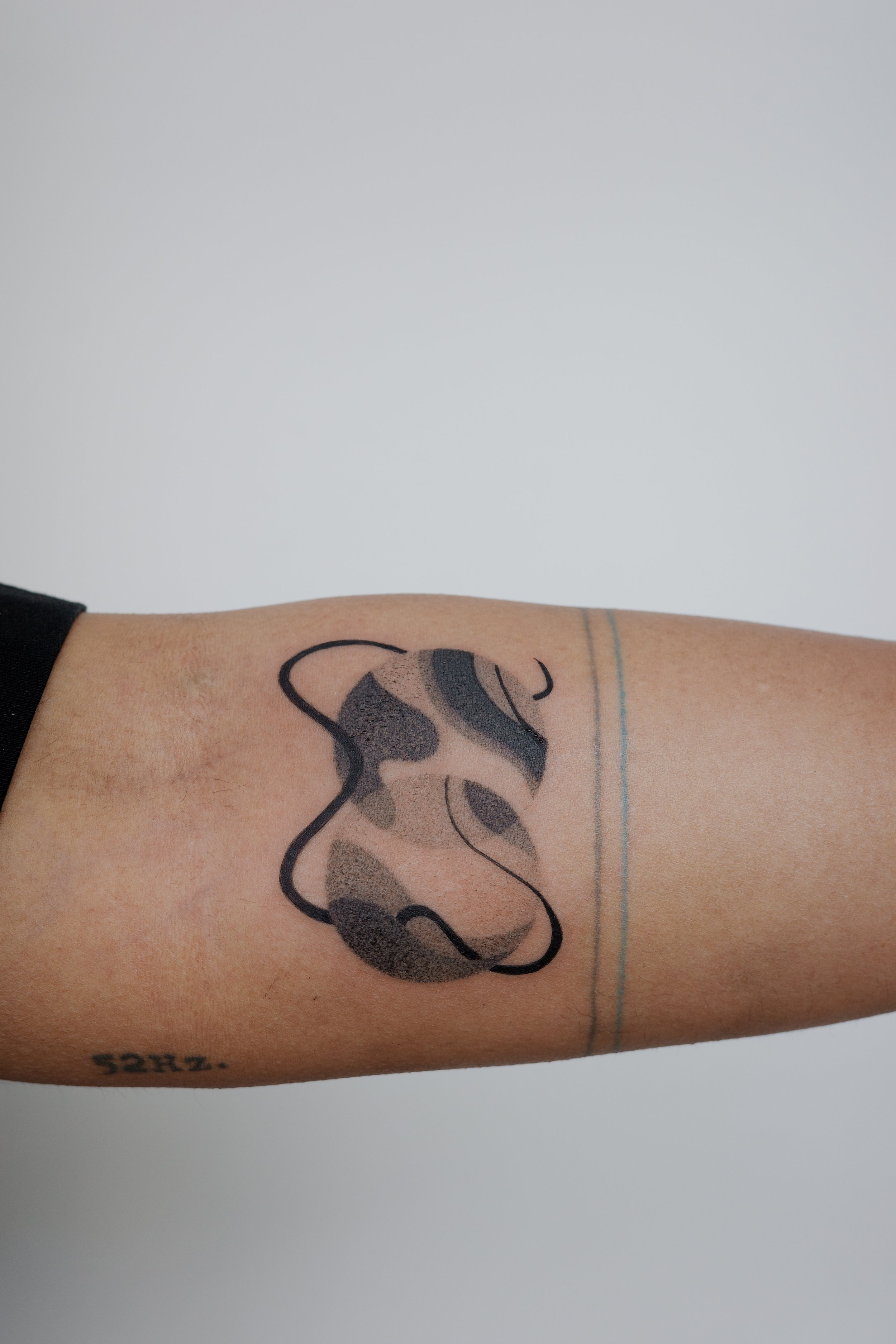 Close-up of a person's forearm with a tattoo of a stylized abstract animal face, along with the words "SPRU" tattooed near the wrist.