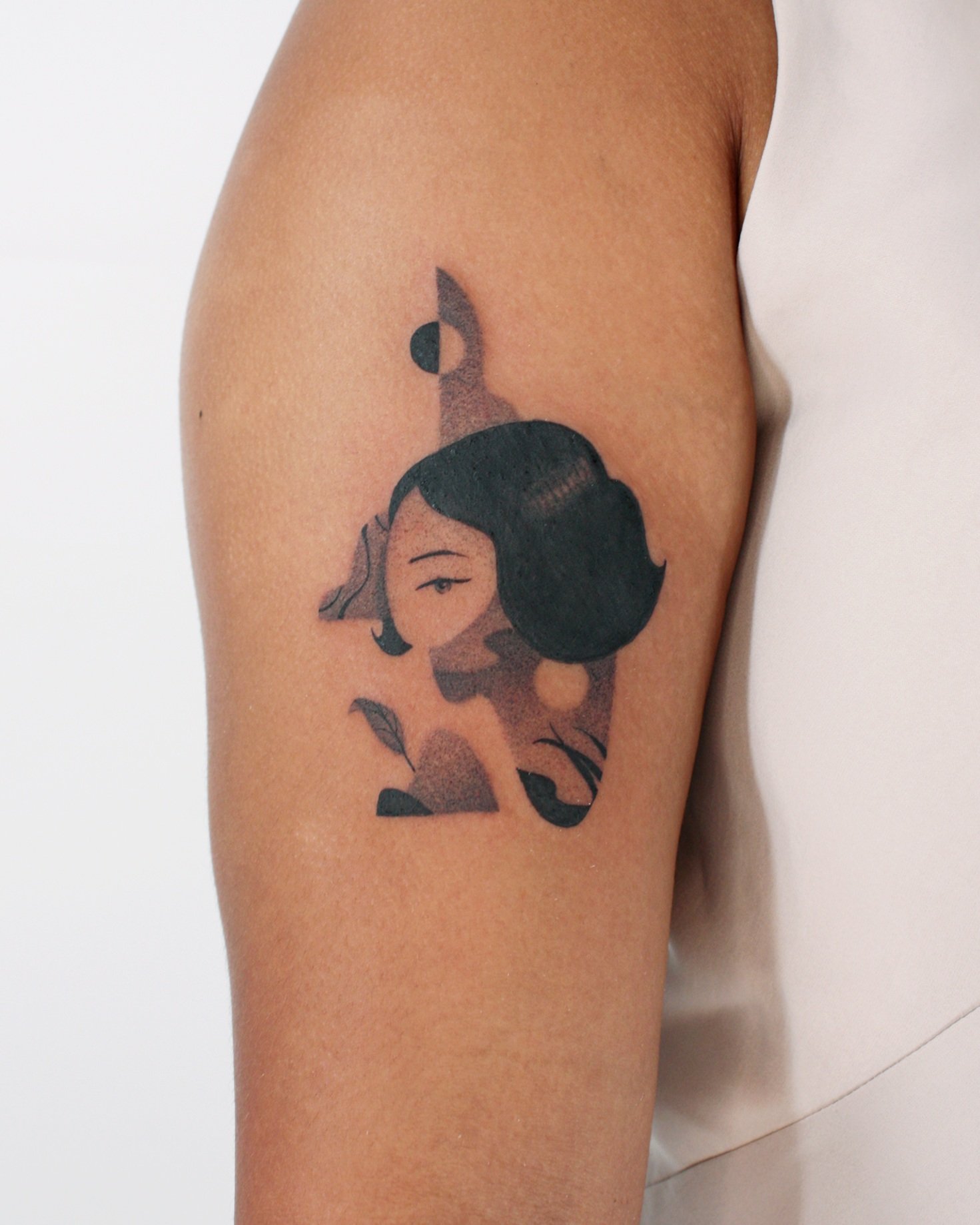 Tattoo of a girl with black hair and a moon on her forehead on a person's upper arm.