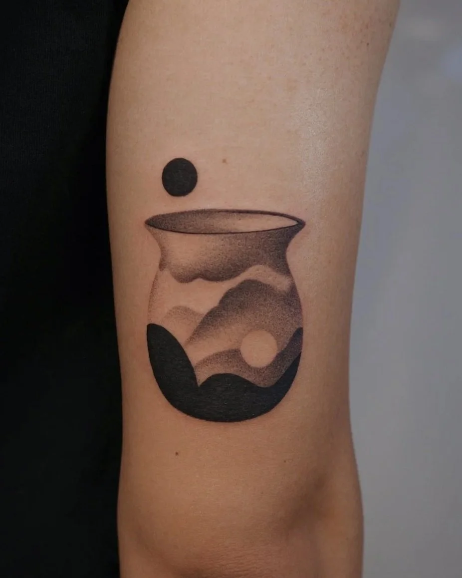 Tattoo of a minimalist landscape inside a glass, with mountains, a sun, and abstract shapes.