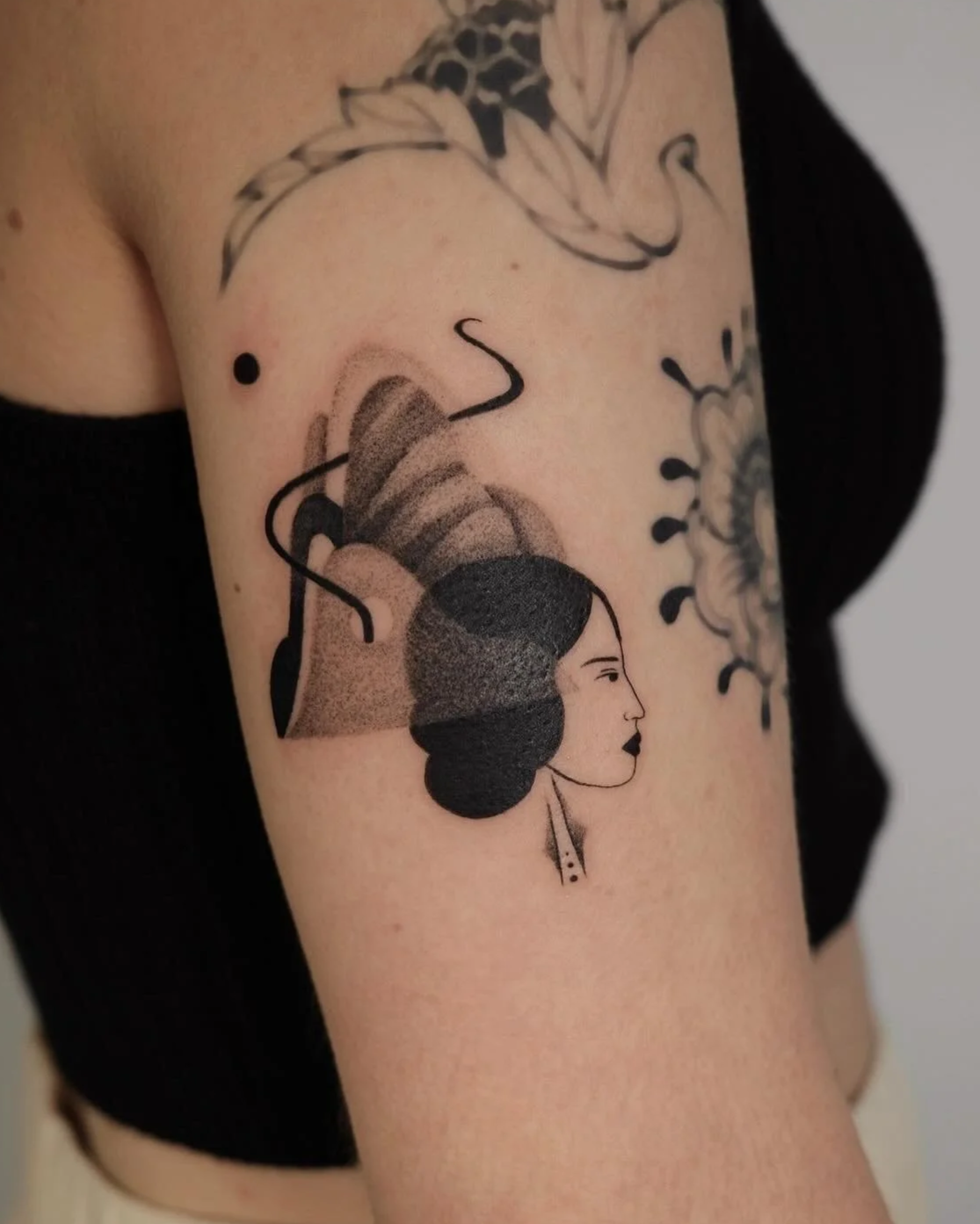 Tattoo of a woman's face in profile with stylized hair, surrounded by abstract lines and shapes, on a person's upper arm.