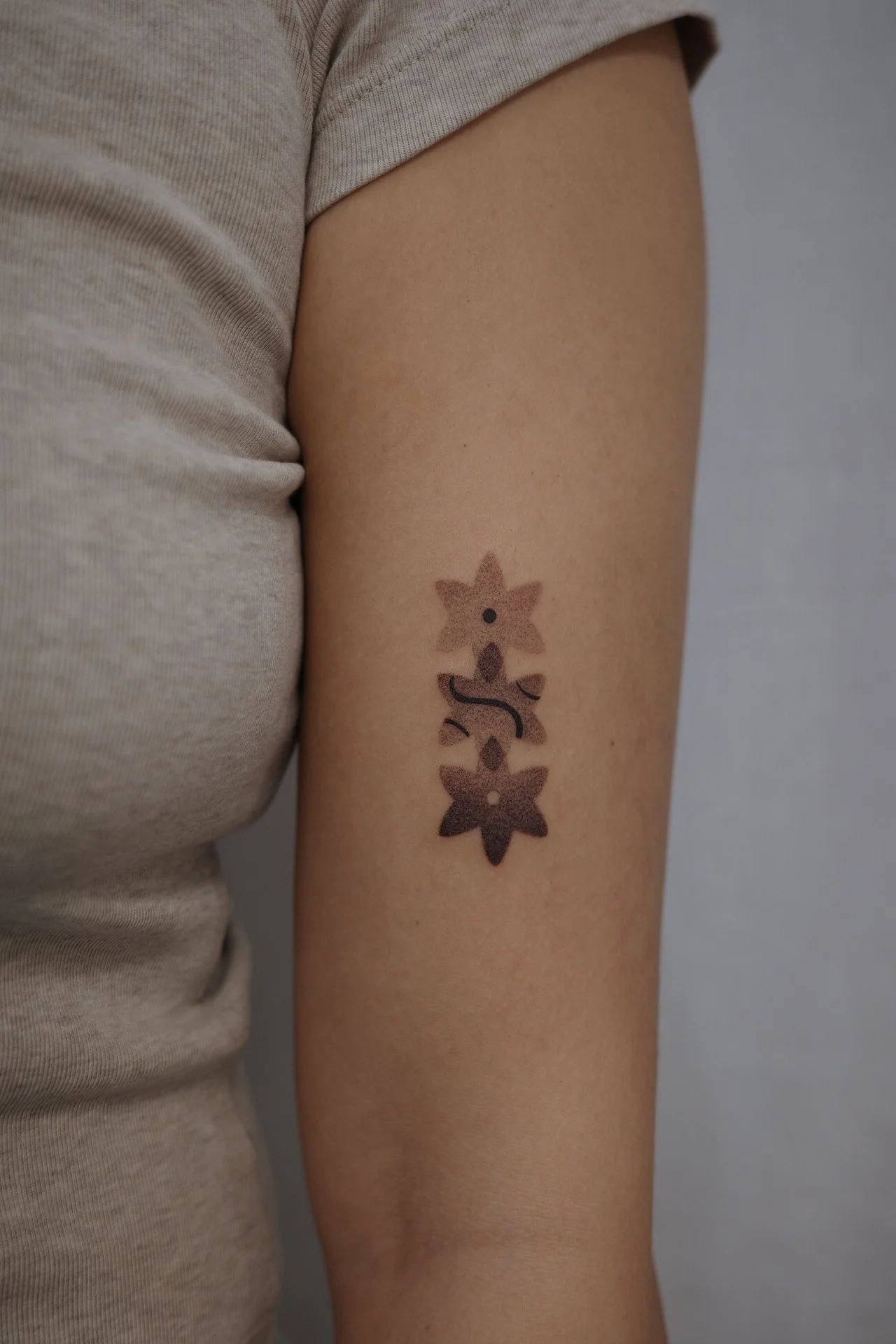 A person's upper arm with a tattoo of three small brown stars connected by a black line.