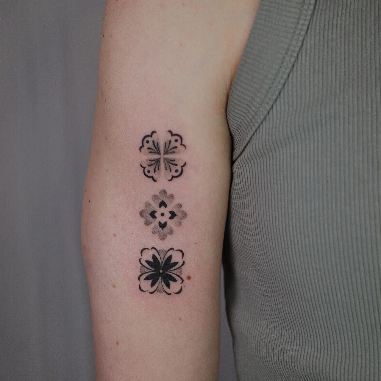 A person's upper arm with three black and gray floral tattoos arranged vertically.
