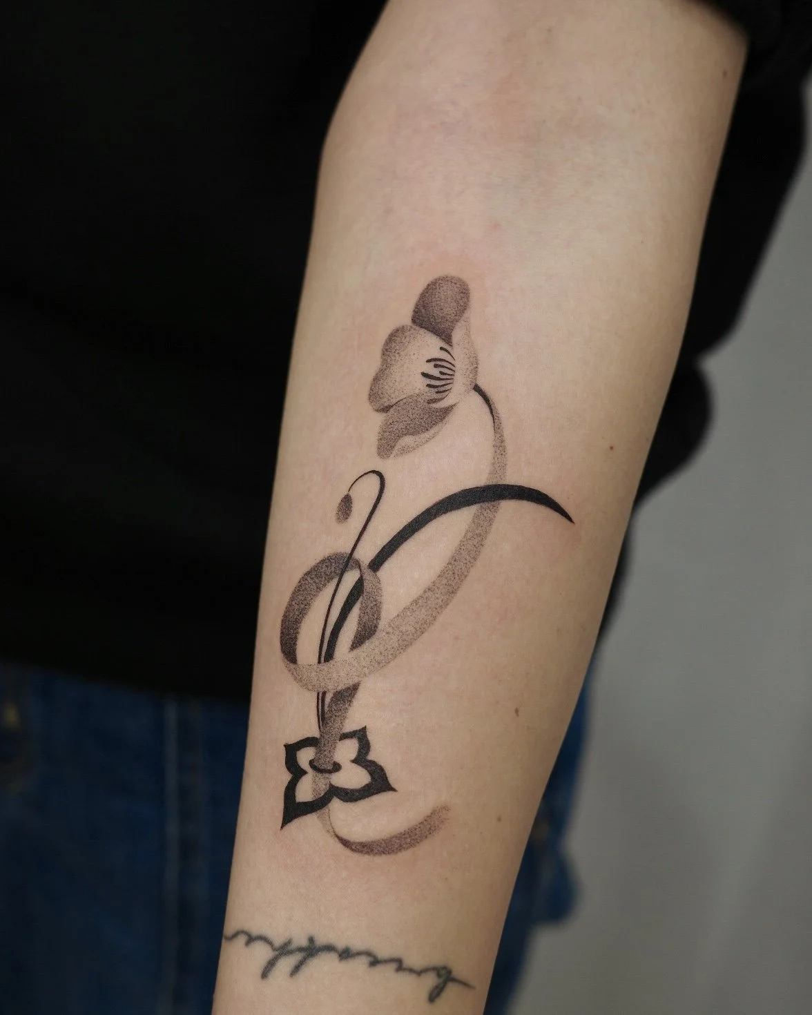 Black outline tattoo of a musical note with a daffodil flower on top, on a person's forearm.
