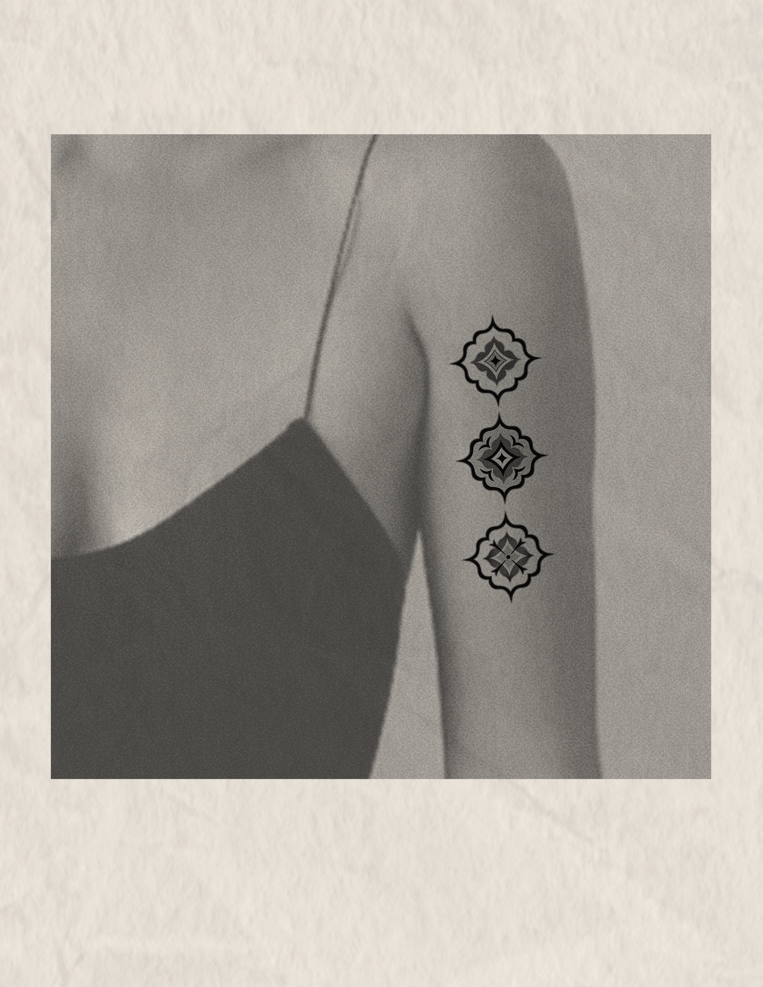 Black and white photograph of a woman's shoulder and arm, with a beaded necklace featuring four ornate, symmetrical designs hanging down.