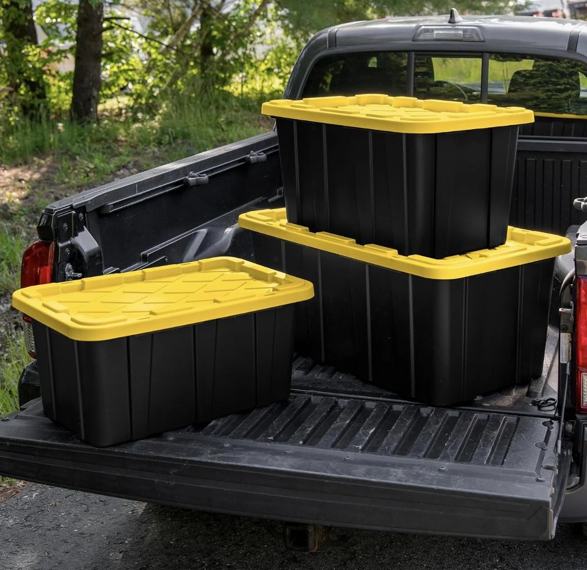 Three black and yellow storage containers in the back of a pickup truck, with a forested area in the background.