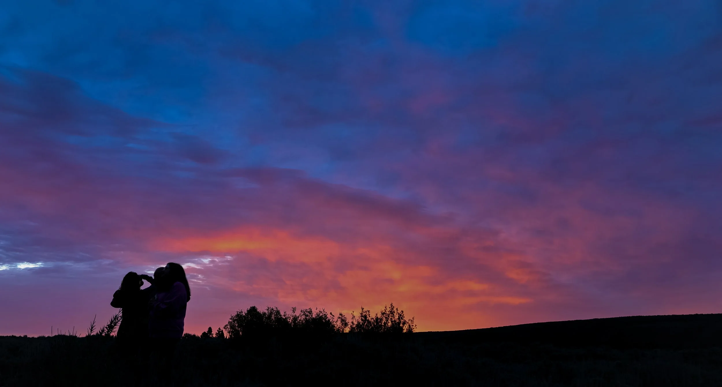 Silhouette of a couple beneath a vibrant purple and orange sunset sky over a quiet landscape