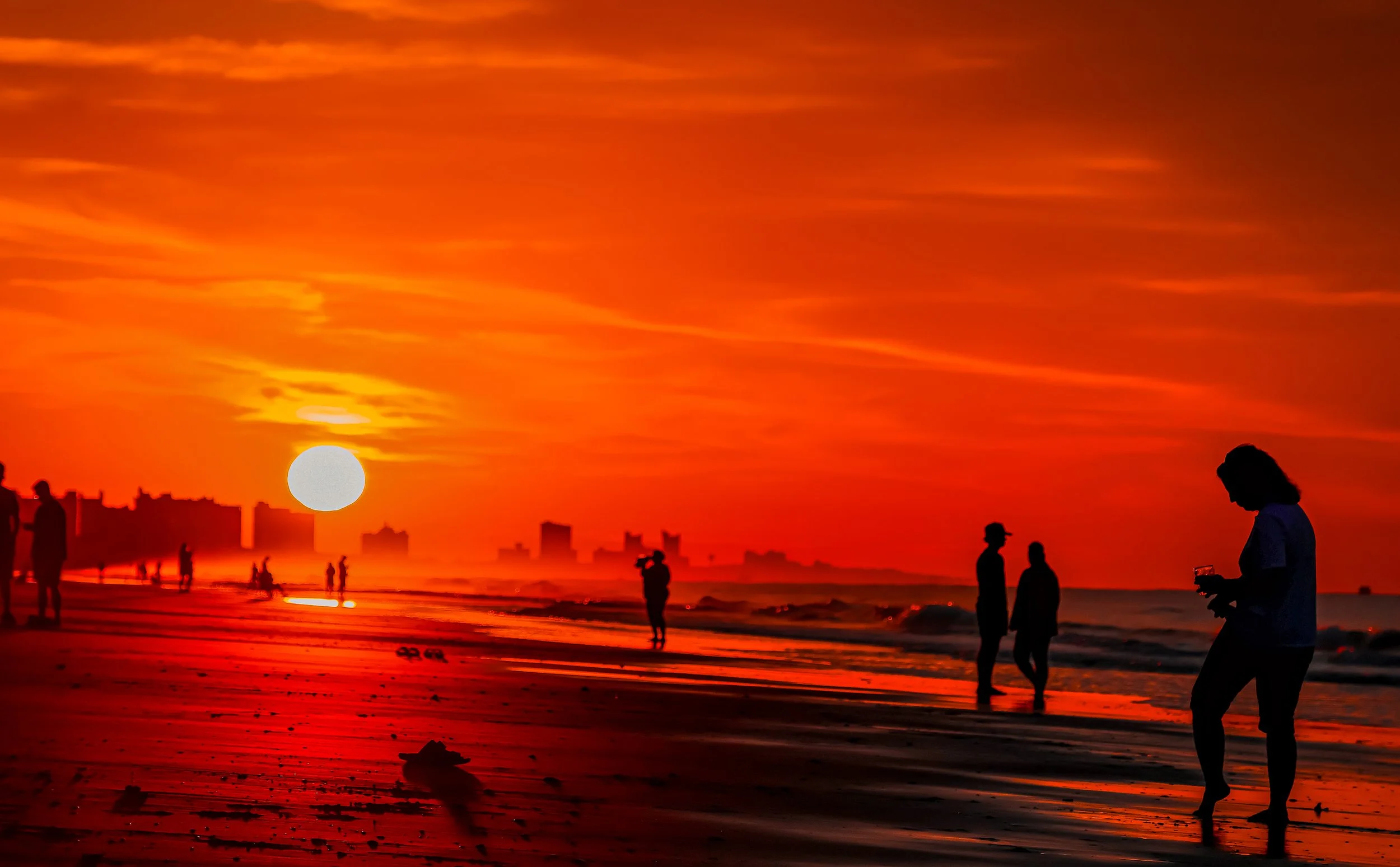Golden sunset over Myrtle Beach with silhouettes of people walking along the shoreline.