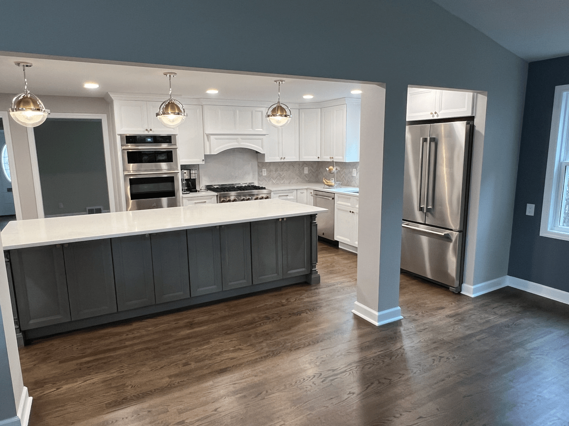 Modern kitchen with white cabinets, stainless steel appliances, a large island with a dark base, pendant lighting, and hardwood flooring.