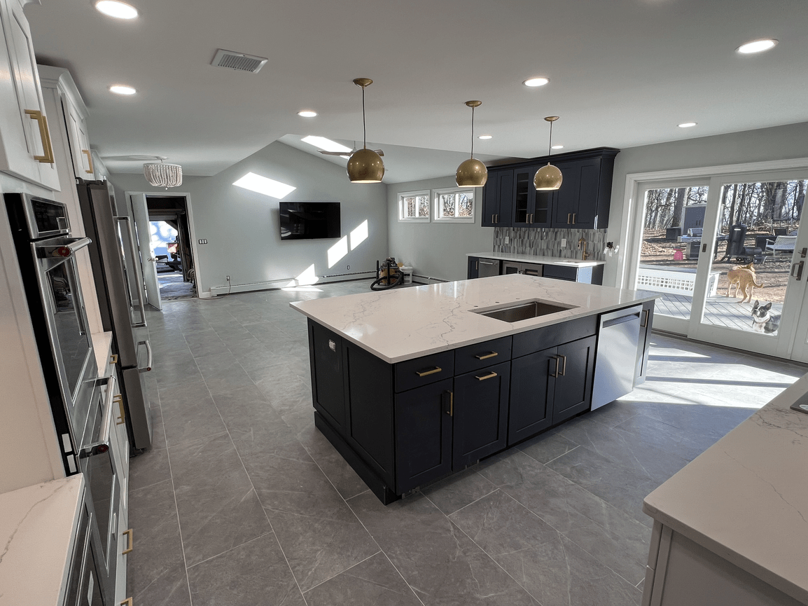 Modern kitchen with dark blue cabinets, white marble island, gray tile flooring, stainless steel appliances, and a sliding glass door leading outside.