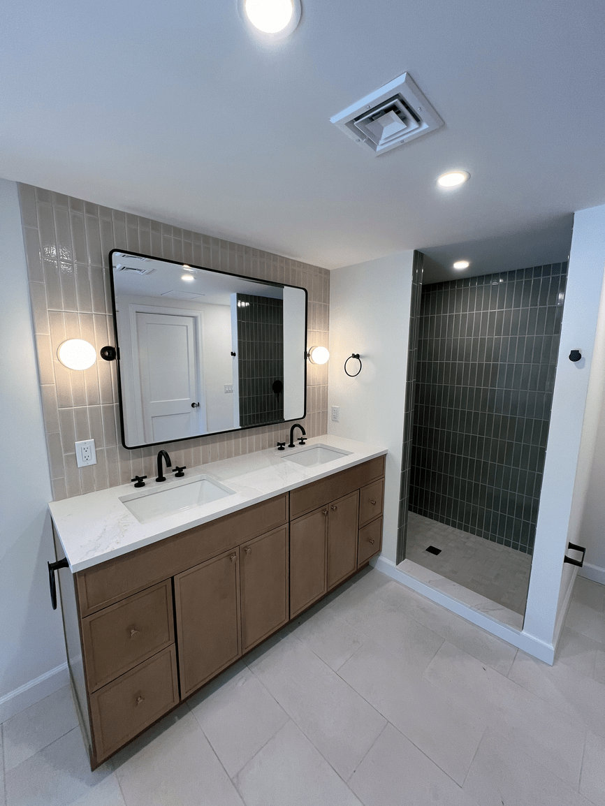 Bathroom with double vanity, large mirror, wall-mounted lights, and a walk-in shower with dark gray tile walls.