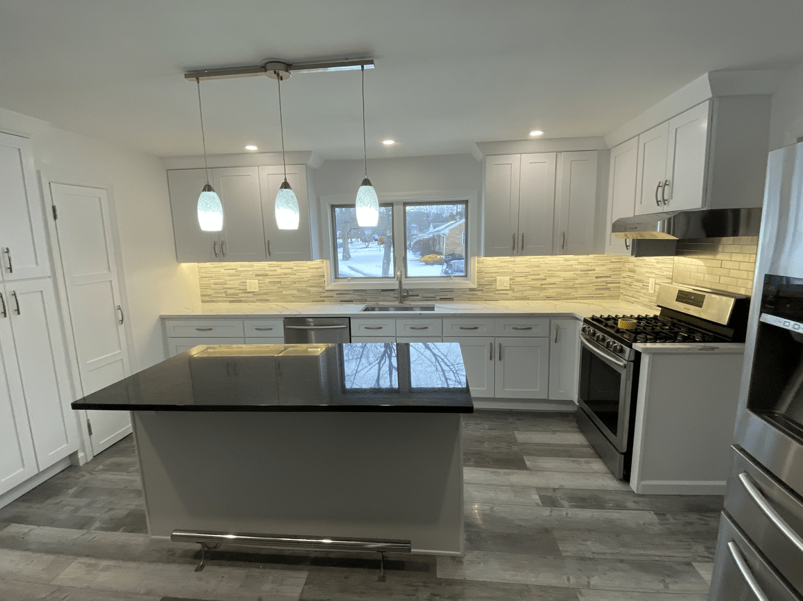 Modern kitchen with white cabinets, gray countertops, stainless steel appliances, a kitchen island with a black countertop, and a tile backsplash. There are three pendant lights hanging above the island and a window above the sink showing an outdoor 