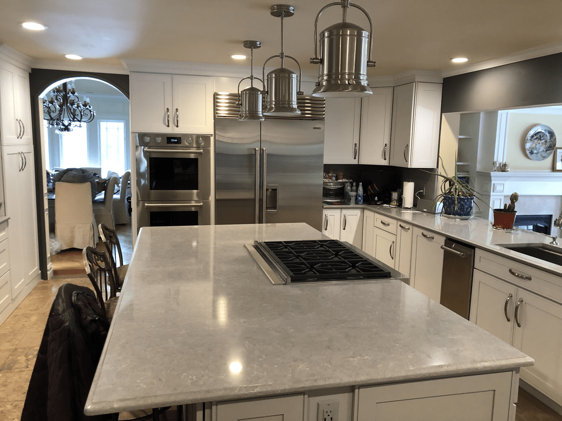 Modern kitchen with white cabinets, stainless steel refrigerator and oven, island with a gas stove, pendant lights, and a view into a dining room with a chandelier.