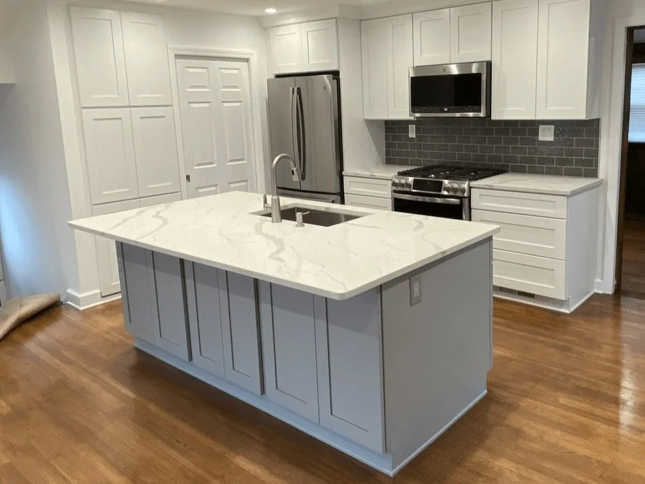 Modern kitchen with white cabinets, stainless steel appliances, gray subway tile backsplash, and a white marble countertop island.