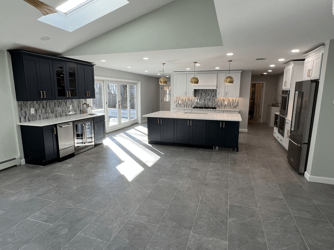 Modern kitchen with dark blue and white cabinets, marble countertops, gray tiled flooring, stainless steel appliances, and pendant lighting, with a sliding glass door leading outside.