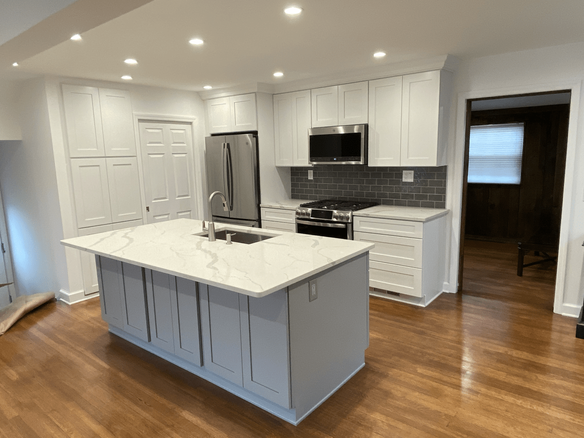 Modern kitchen with white cabinets, stainless steel appliances, a marble island, and hardwood floors.