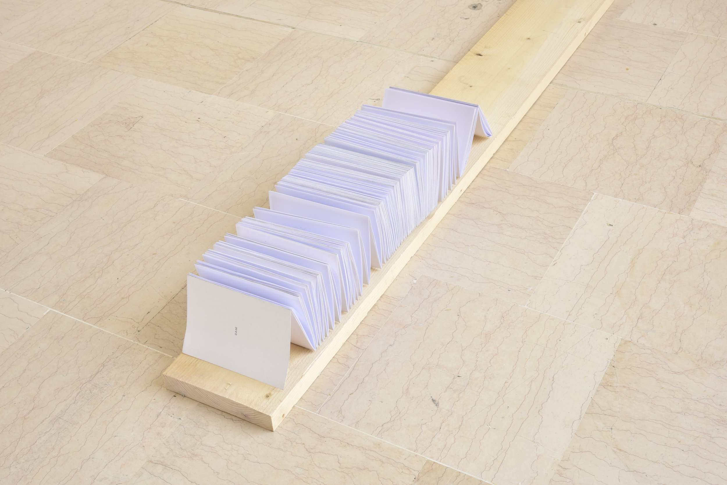 Une rangée de feuilles blanches pliées, placées sur une planche en bois en longueur, située sur un sol en carrelage beige.