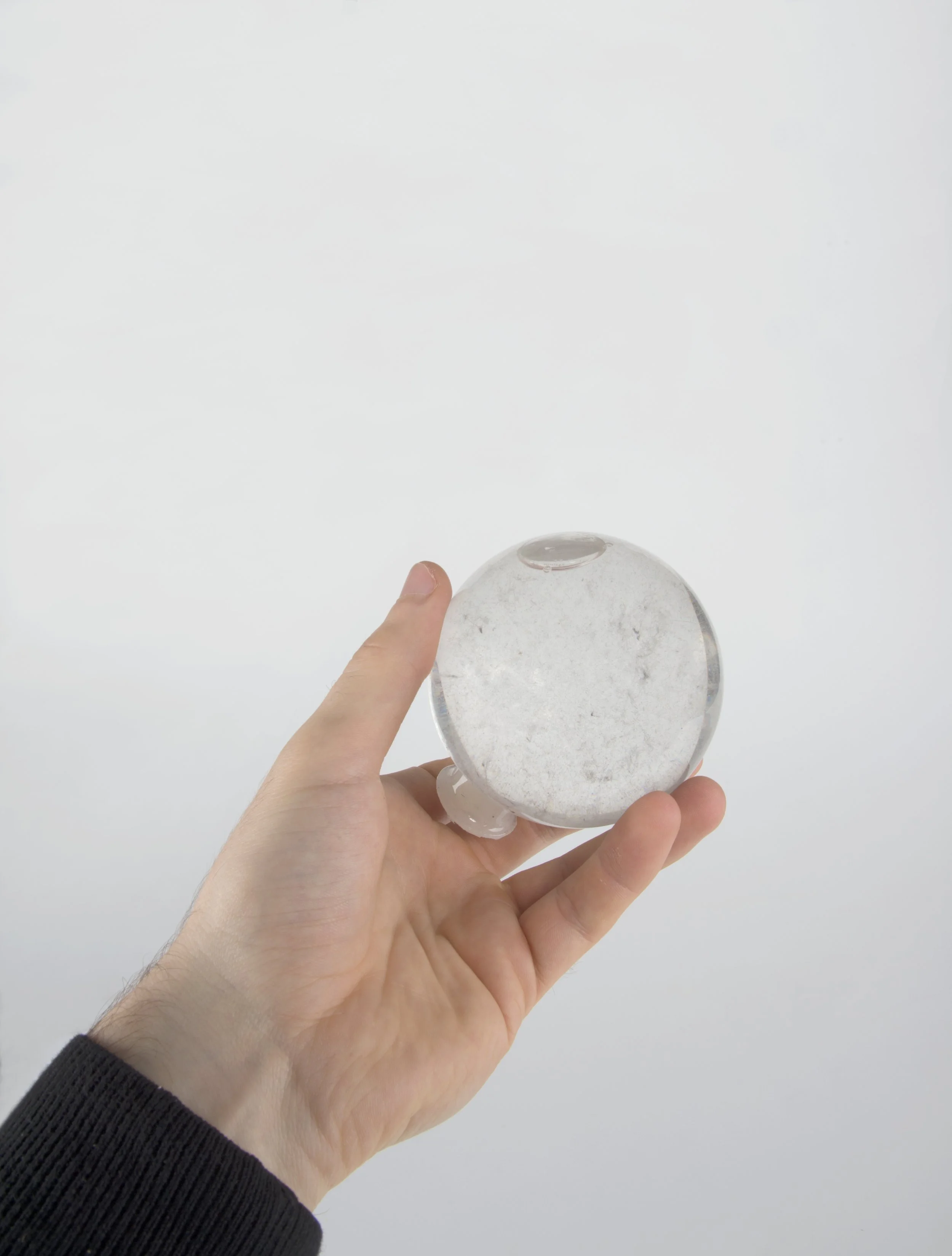 Main tenant une boule de verre transparente contenant de la poussière contre un fond blanc.