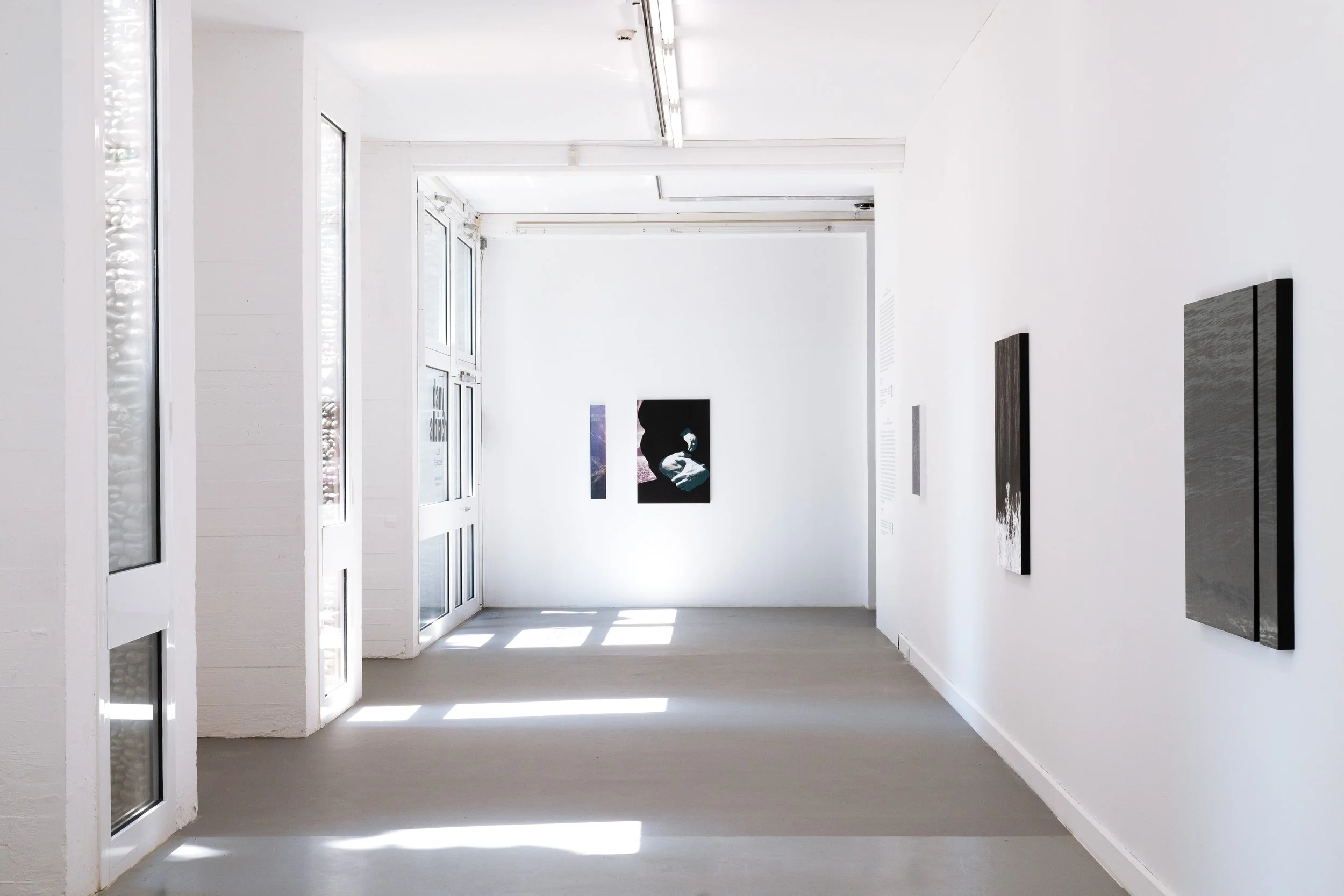 Une salle d'exposition d'art moderne avec des œuvres accrochées aux murs blancs et une lumière naturelle provenant de fenêtres ouvertes. Vila Arson