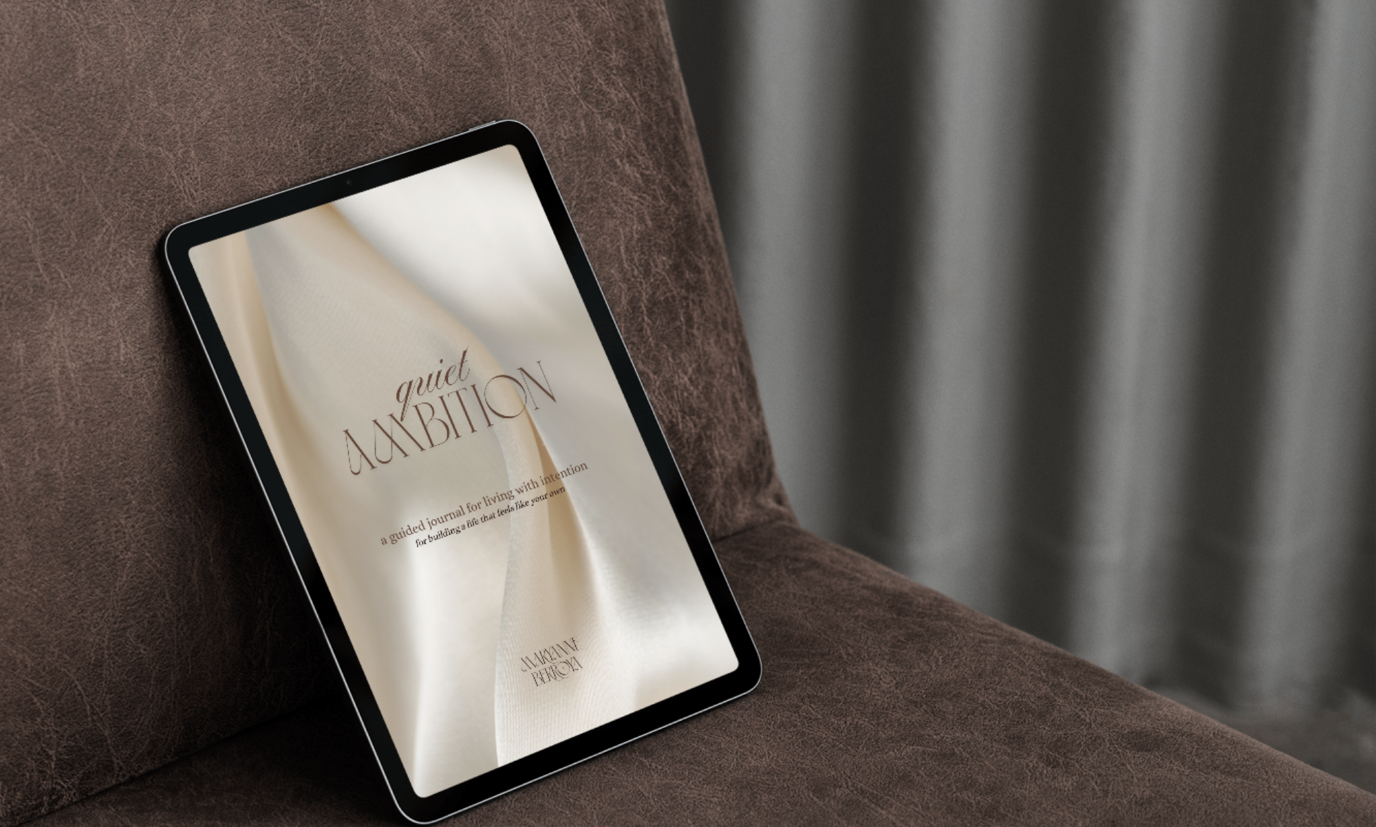 An electronic tablet resting on a brown textured surface, displaying the cover of a guided journal called "Quiet Ambition" with a cream-colored background and elegant font.