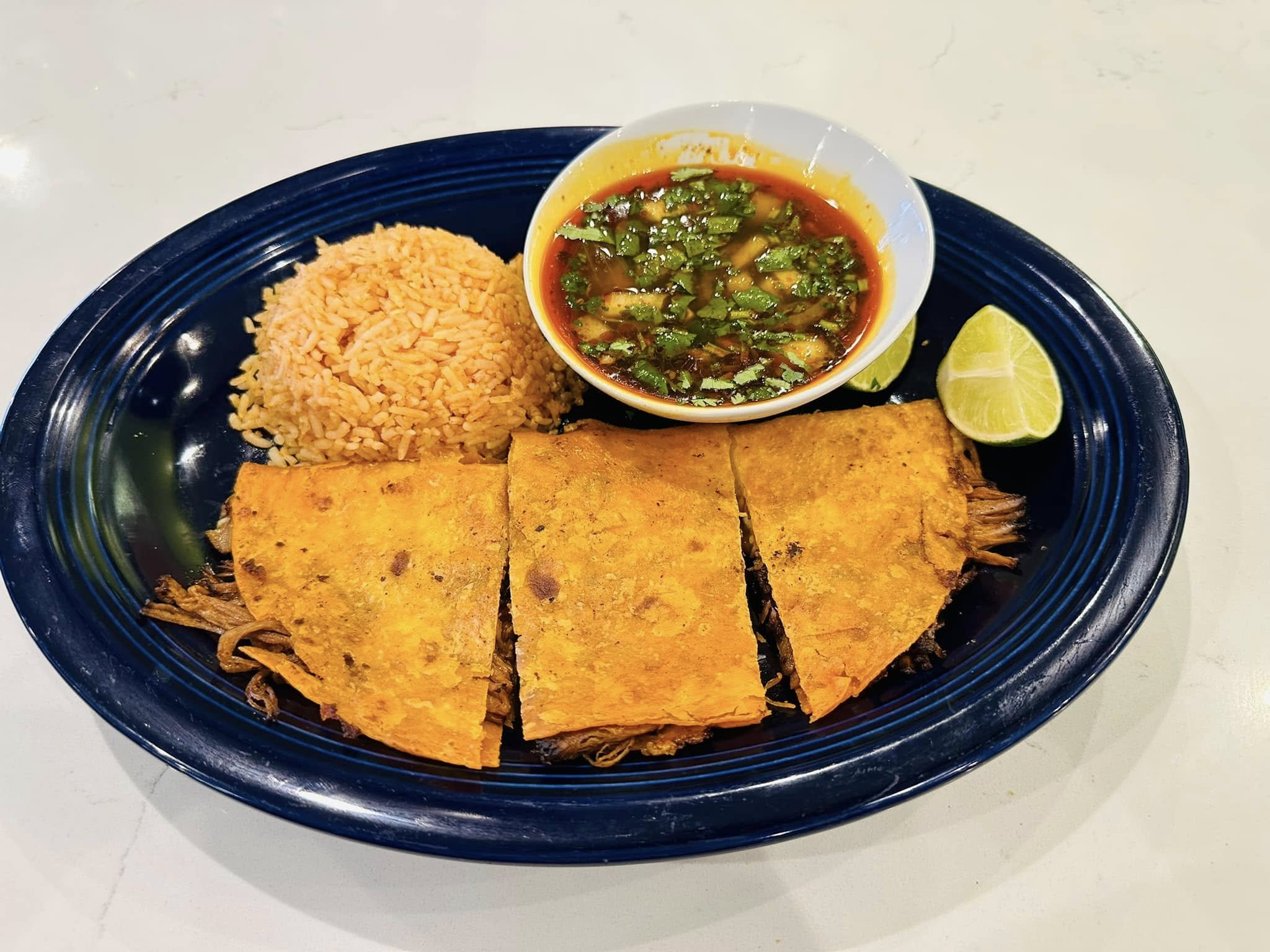 Plate with rice, grilled fish, and lime wedges, served with a bowl of sauce containing chopped green herbs and chili peppers.