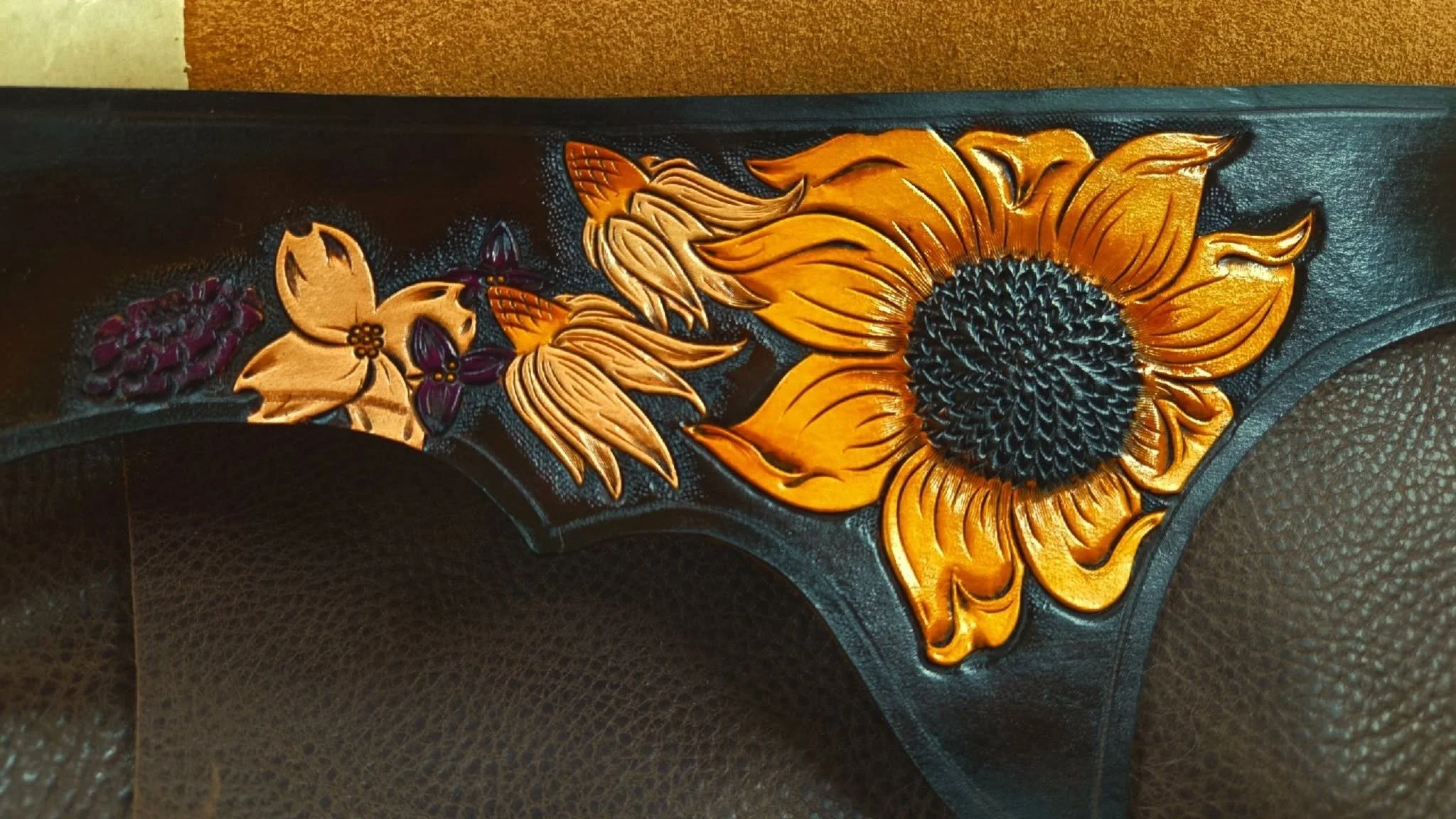 Leather firearm grip with sunflower, butterfly, and grape leaf embossed design in gold and purple colors.