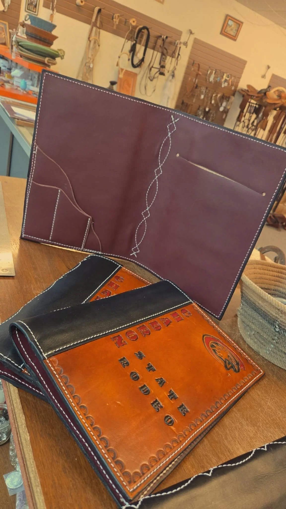 Open leather wallet displaying card slots on the right side and organizational sections on the left side, with other leather wallets and items on the table in the background.