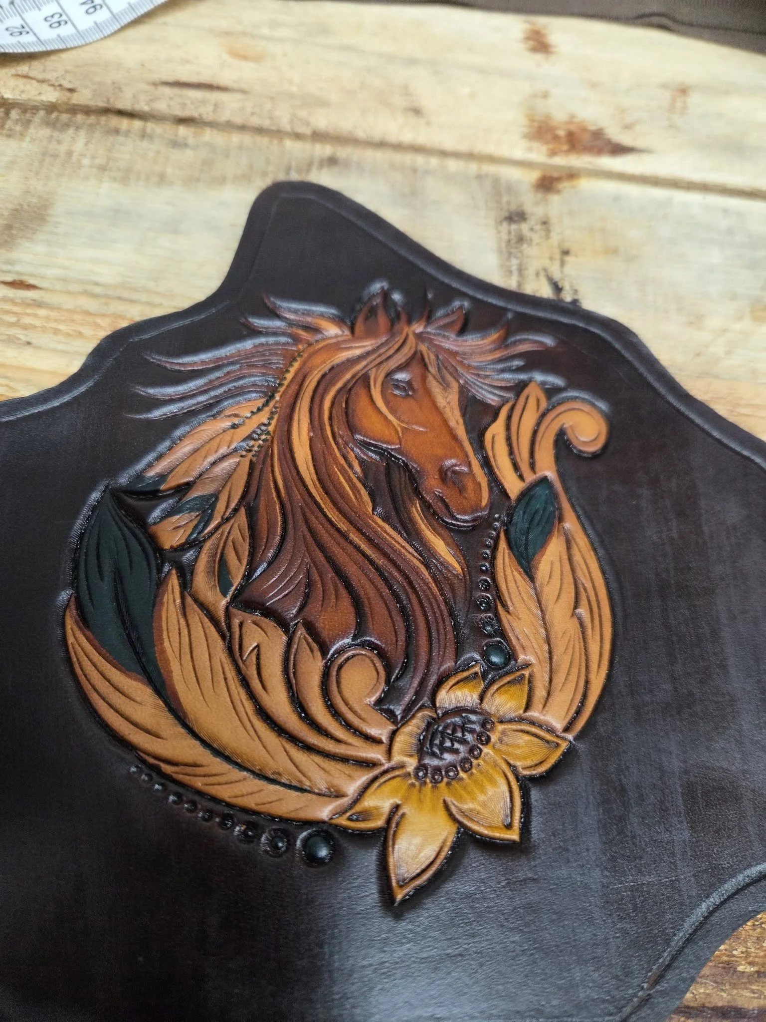 Leather plaque with a embossed or carved image of a horse's head surrounded by floral and leaf designs.
