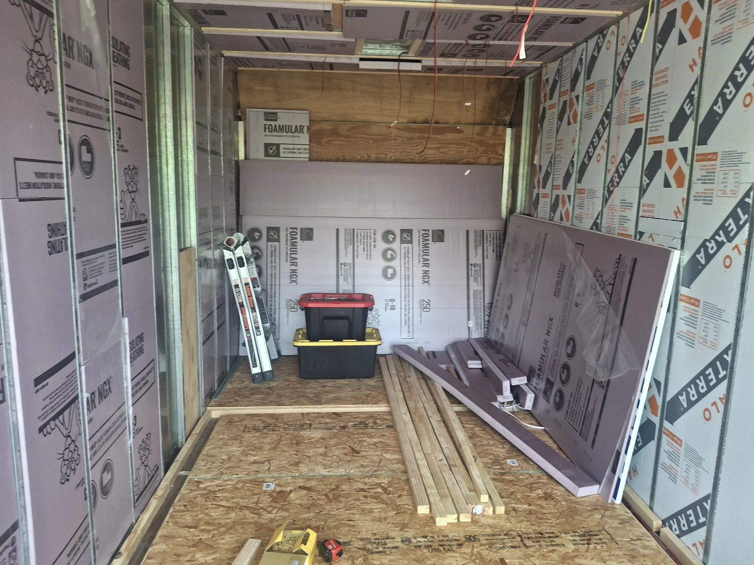 Progress on a DIY box truck conversion showing insulated walls, subfloor installation, and electrical wiring for a four-season off-grid stealth RV and mobile content creation studio.