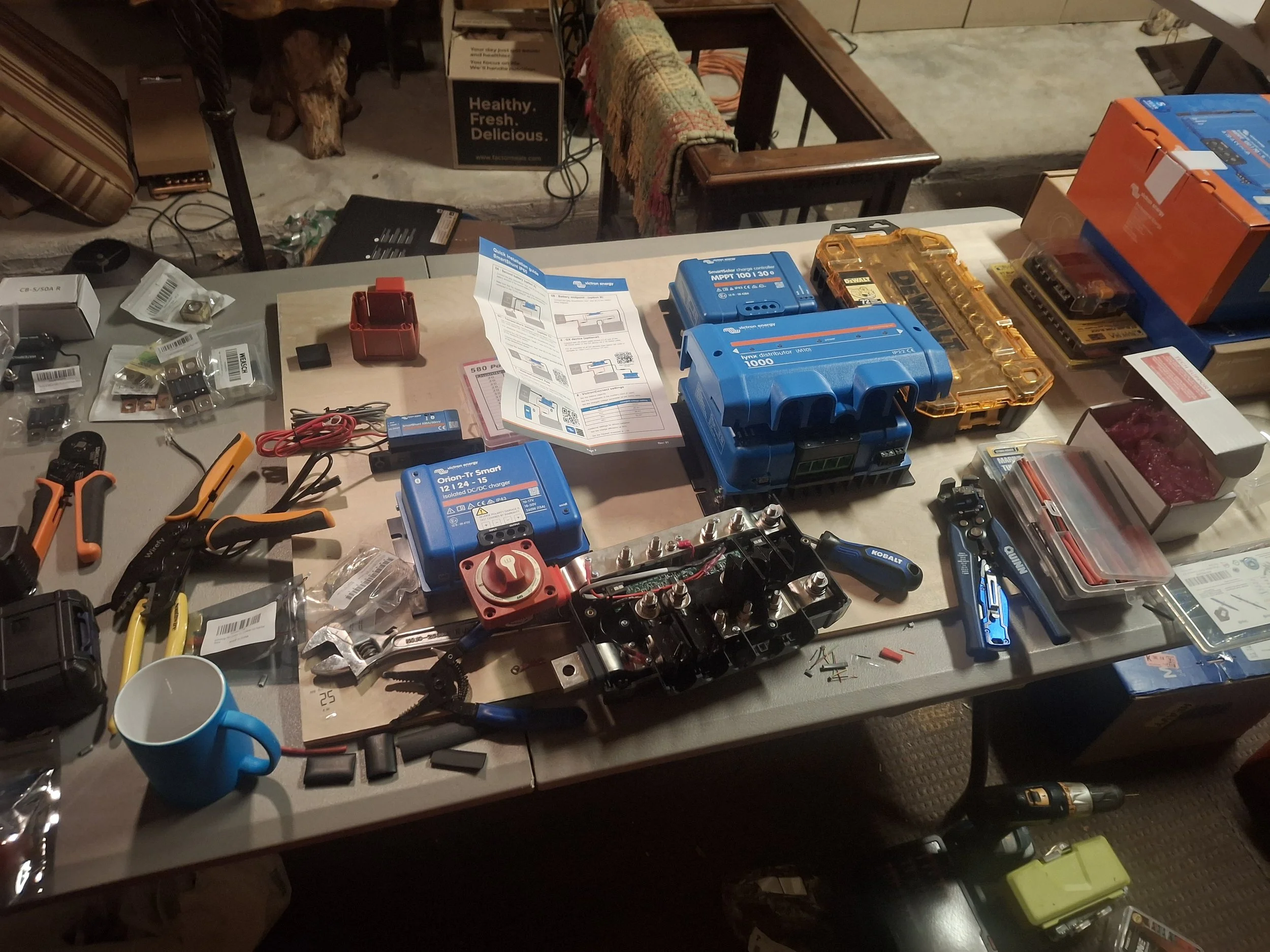 Workbench with Victron Energy components, electrical tools, and wiring used to build a custom 24-volt off-grid solar power system for a DIY Isuzu NPR box truck conversion and mobile storytelling studio.