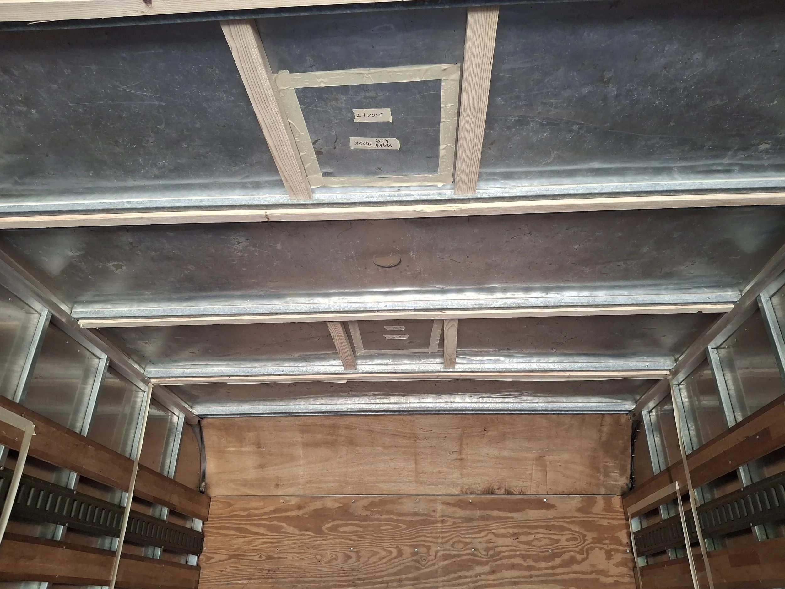 Ceiling framing inside an Isuzu NPR box truck conversion showing wiring routes, roof supports, and preparation for insulation, MaxxAir roof fan installation, and a custom off-grid RV interior.