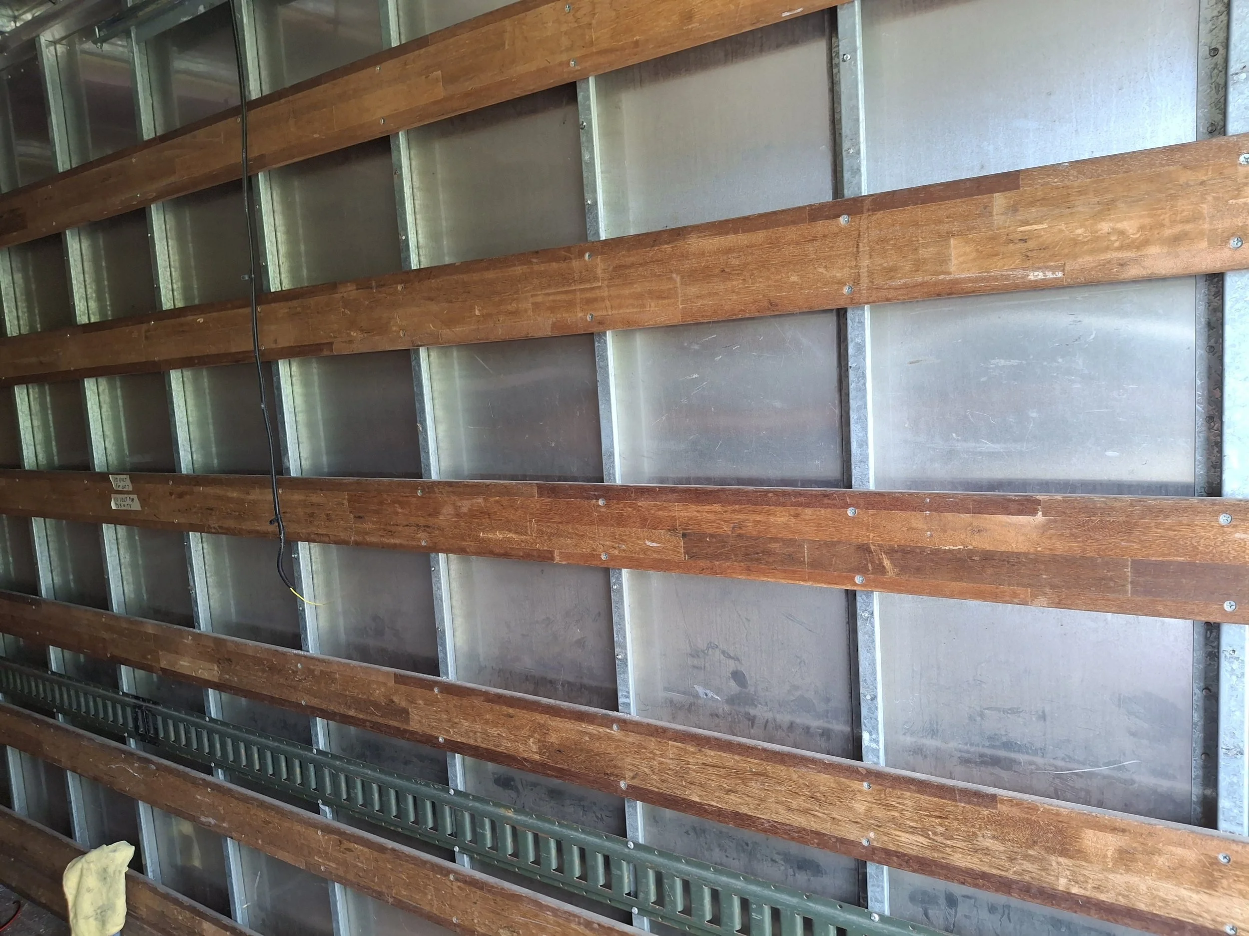 Steel wall framing inside a 20-foot box truck during a DIY RV conversion. Interior structure prepared for insulation, electrical wiring, cabinetry, and a four-season off-grid camper build.