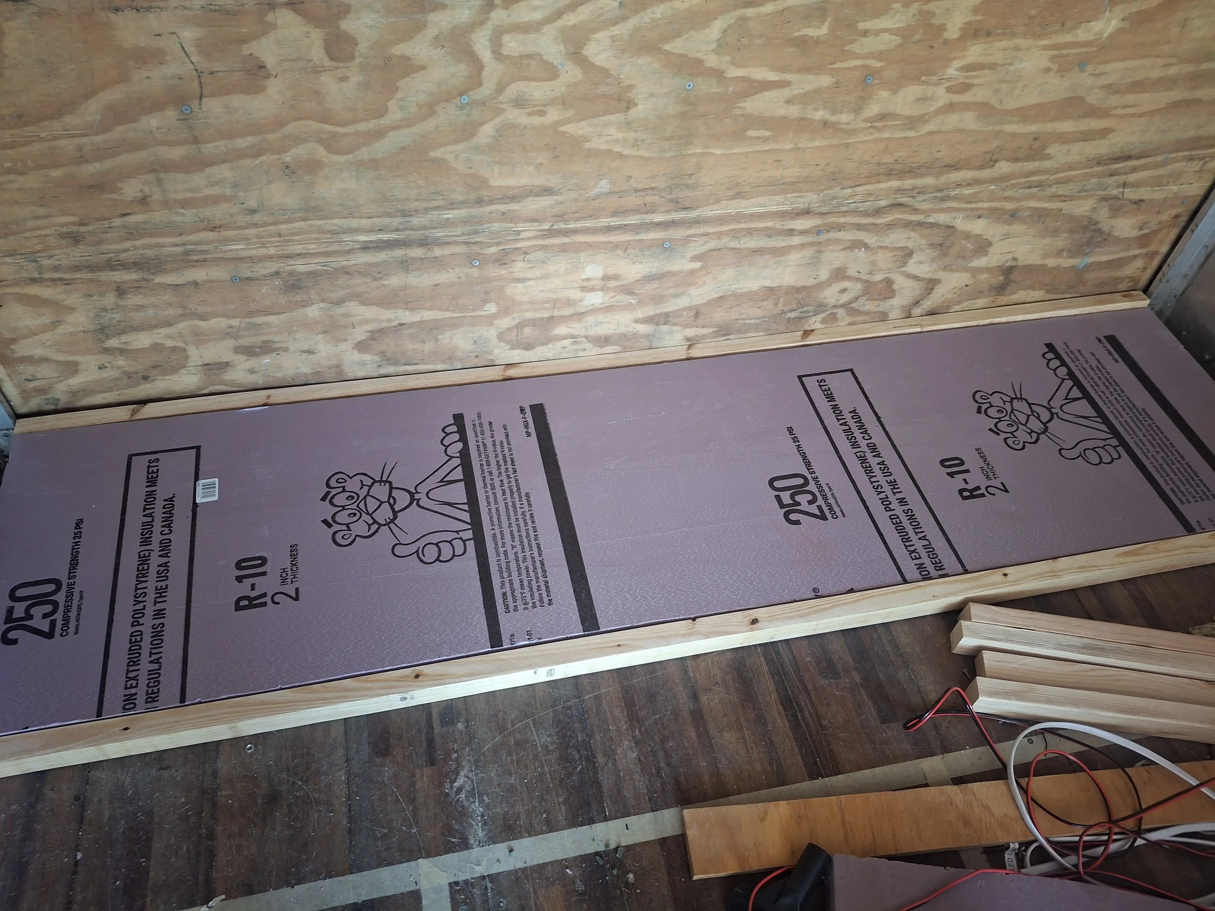Subfloor installation inside a DIY truck camper conversion featuring rigid foam insulation, electrical wiring channels, and wood framing for a four-season off-grid RV build.