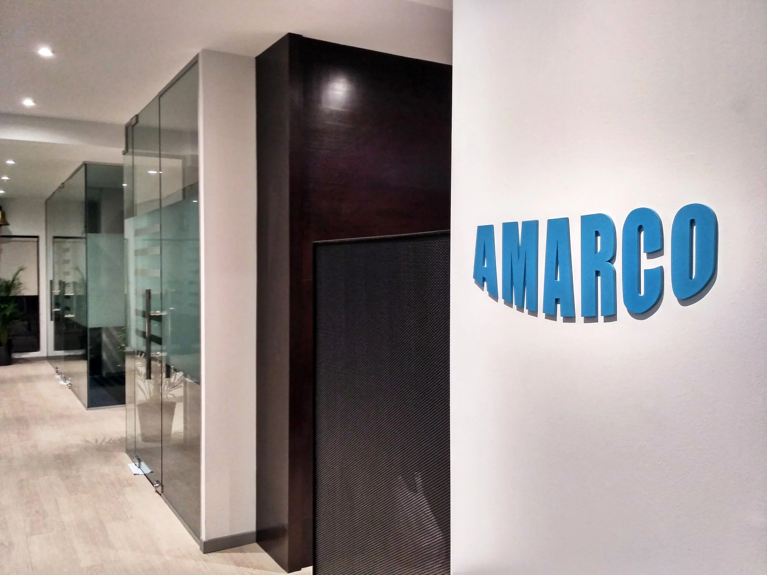 Modern office hallway with glass walls and "AMARCO" sign on white wall