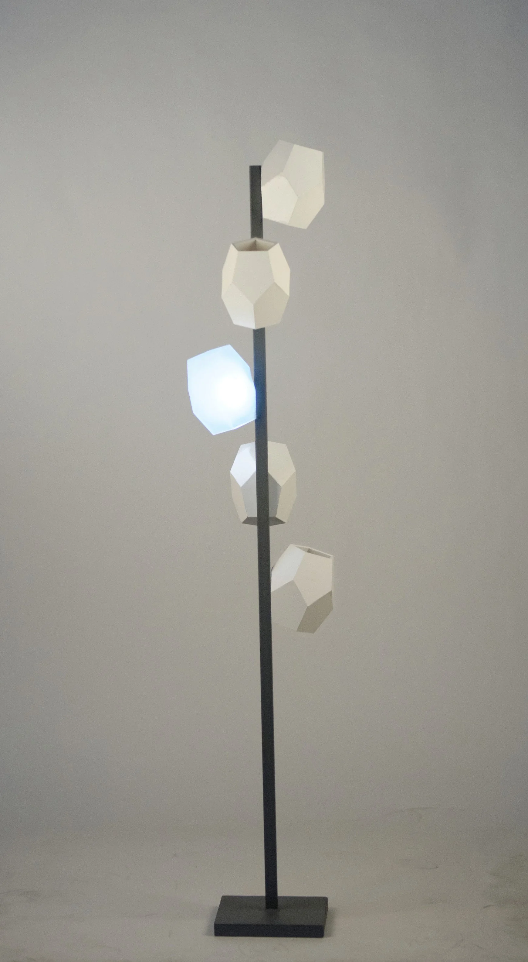 Modern floor lamp with geometric white shades and a black metal base on a gray background.