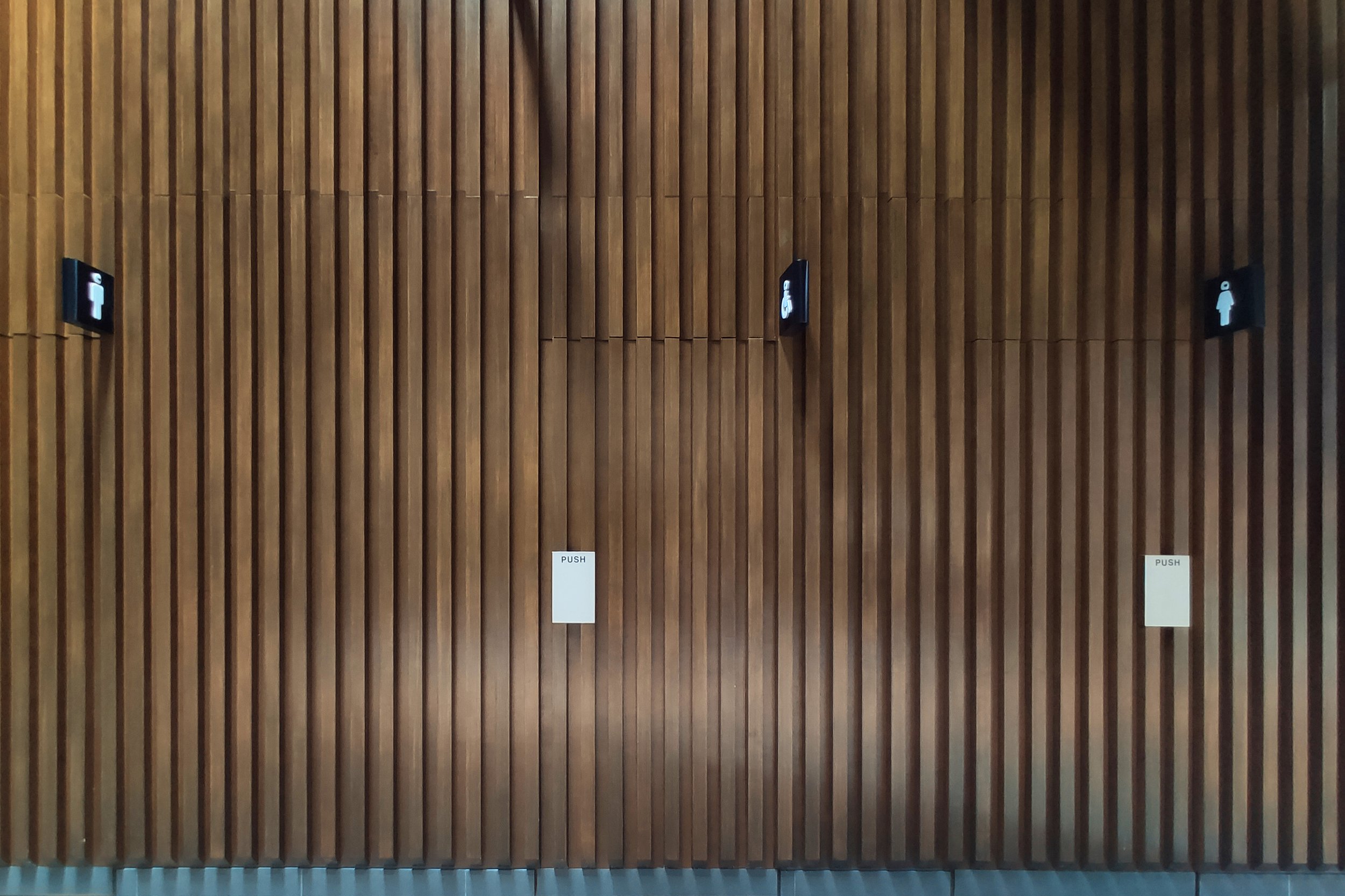 Wooden wall with vertical slats, two restroom signs, and "push" signs on doors.