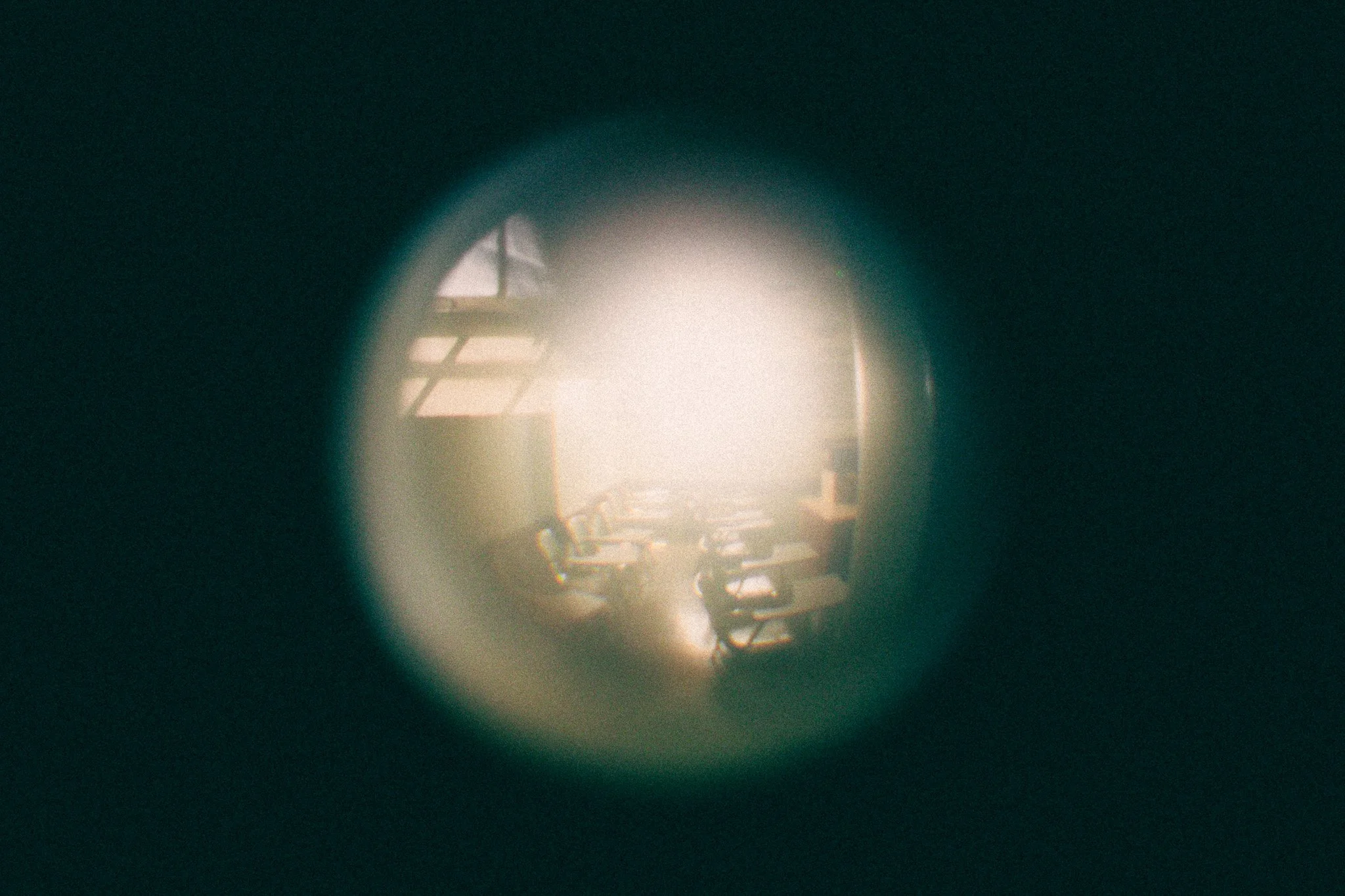 Light shining through a round opening revealing a dim interior with chairs and window with grid pattern.