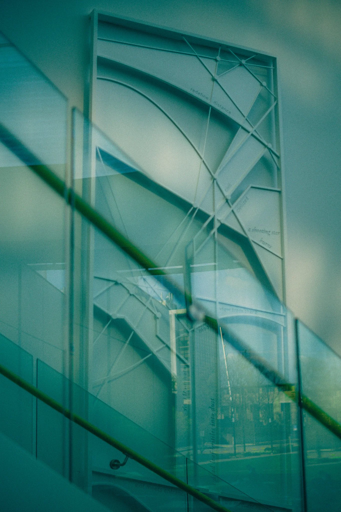Glass building with reflections of a staircase and sky, blurred with a greenish tint.