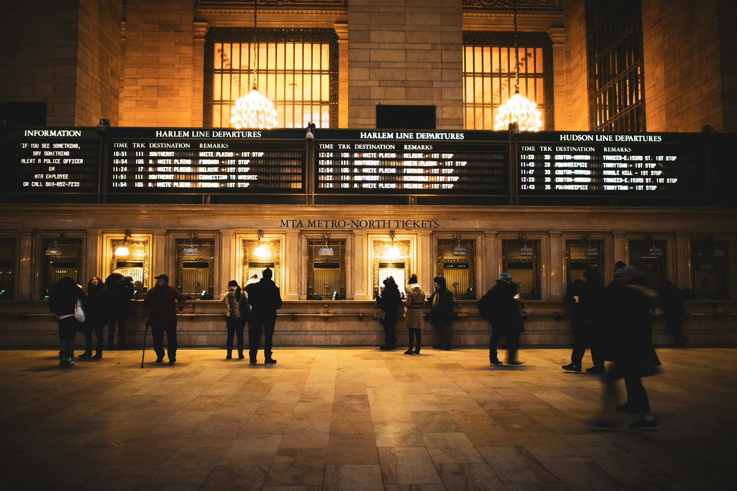 People waiting at a the display board at Grand Central Station with electronic departure boards displaying train times and destinations.