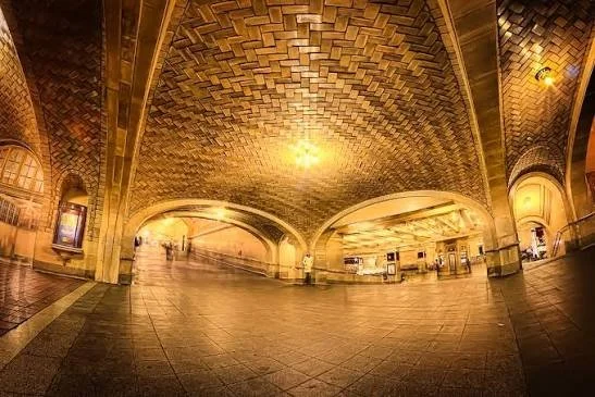 Underground historic vaulted ceiling, tiled design, and tiled floors, illuminated by warm yellow lighting at Grand Central Station. A great place for travelers to meet and have fun.
