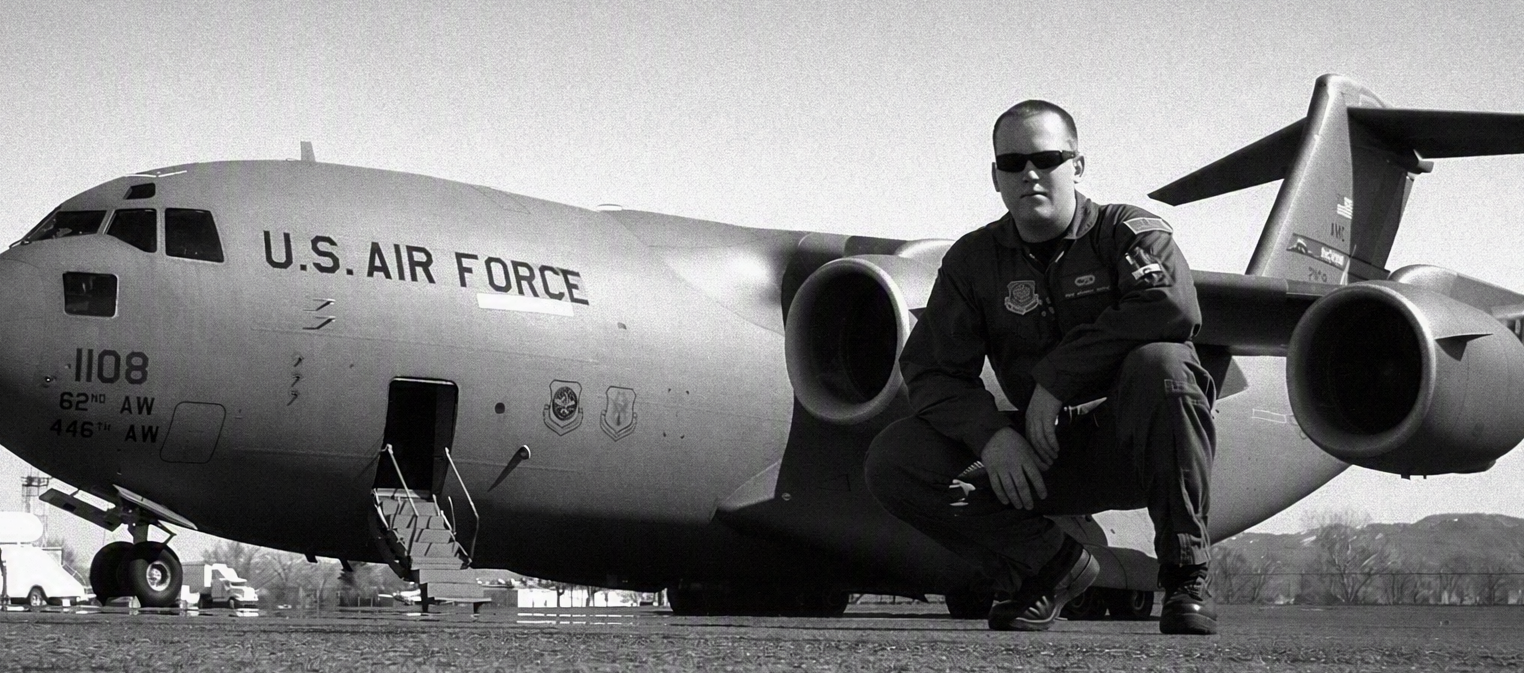 A U.S. Air Force personnel kneeling in front of a military cargo plane on the tarmac.