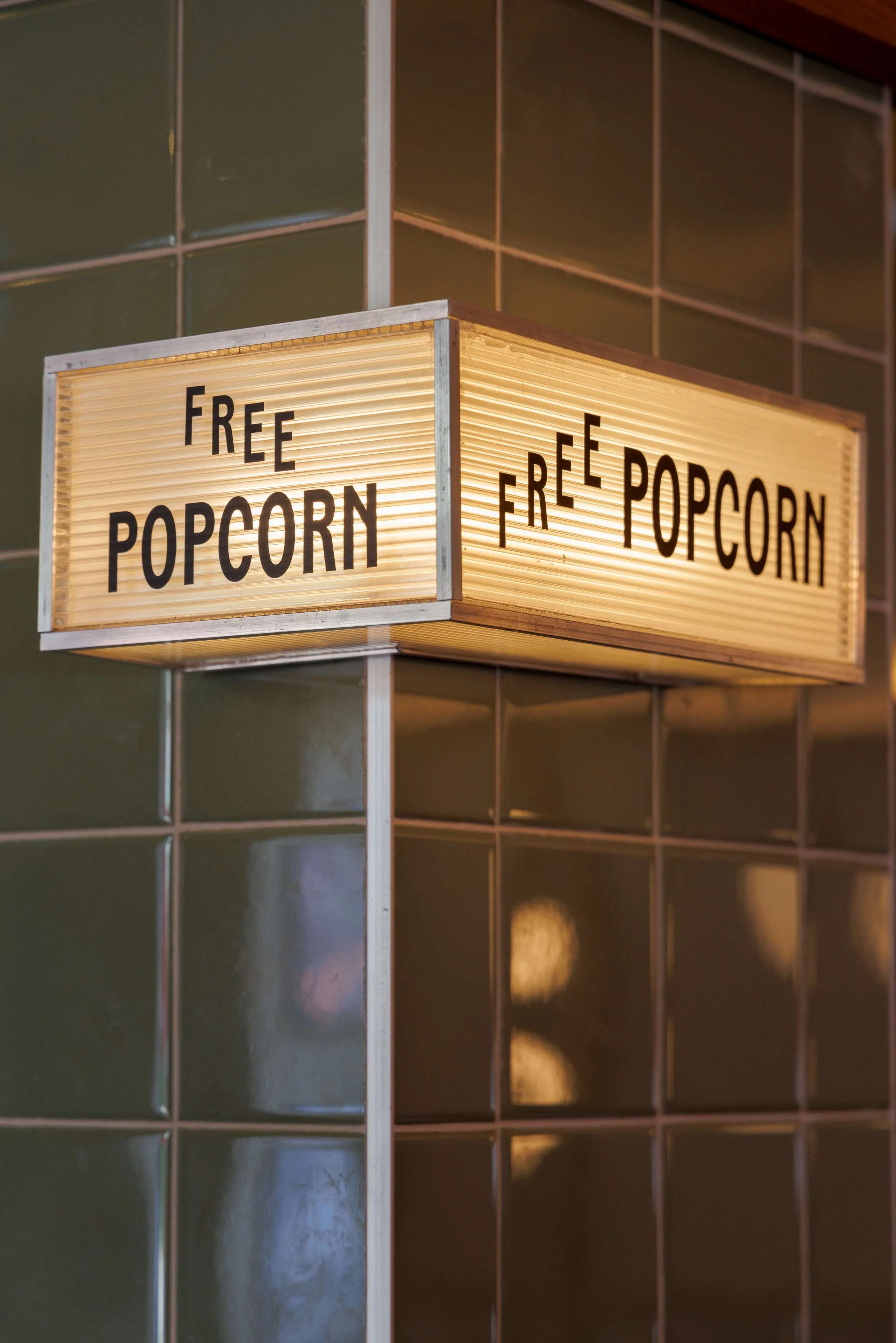 marquee sign on a green tile wall reading free popcorn