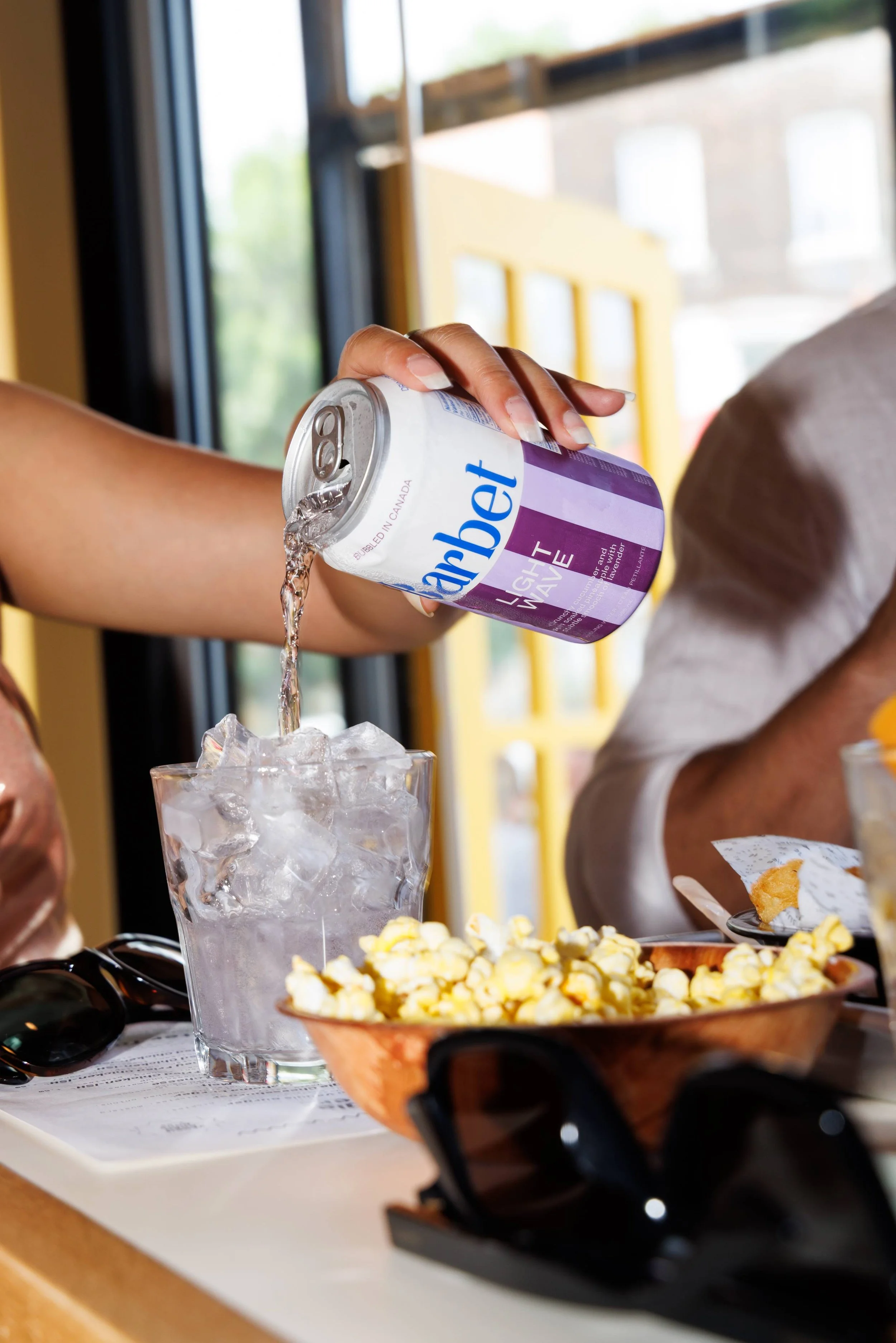 Hand pouring a can of Barbet soda into a glass on a bar