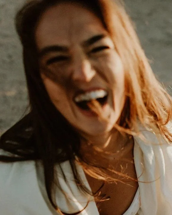 Stephanie Weden, mother, teacher, and founder of WedenMG, laughing with her hair blowing over her face.