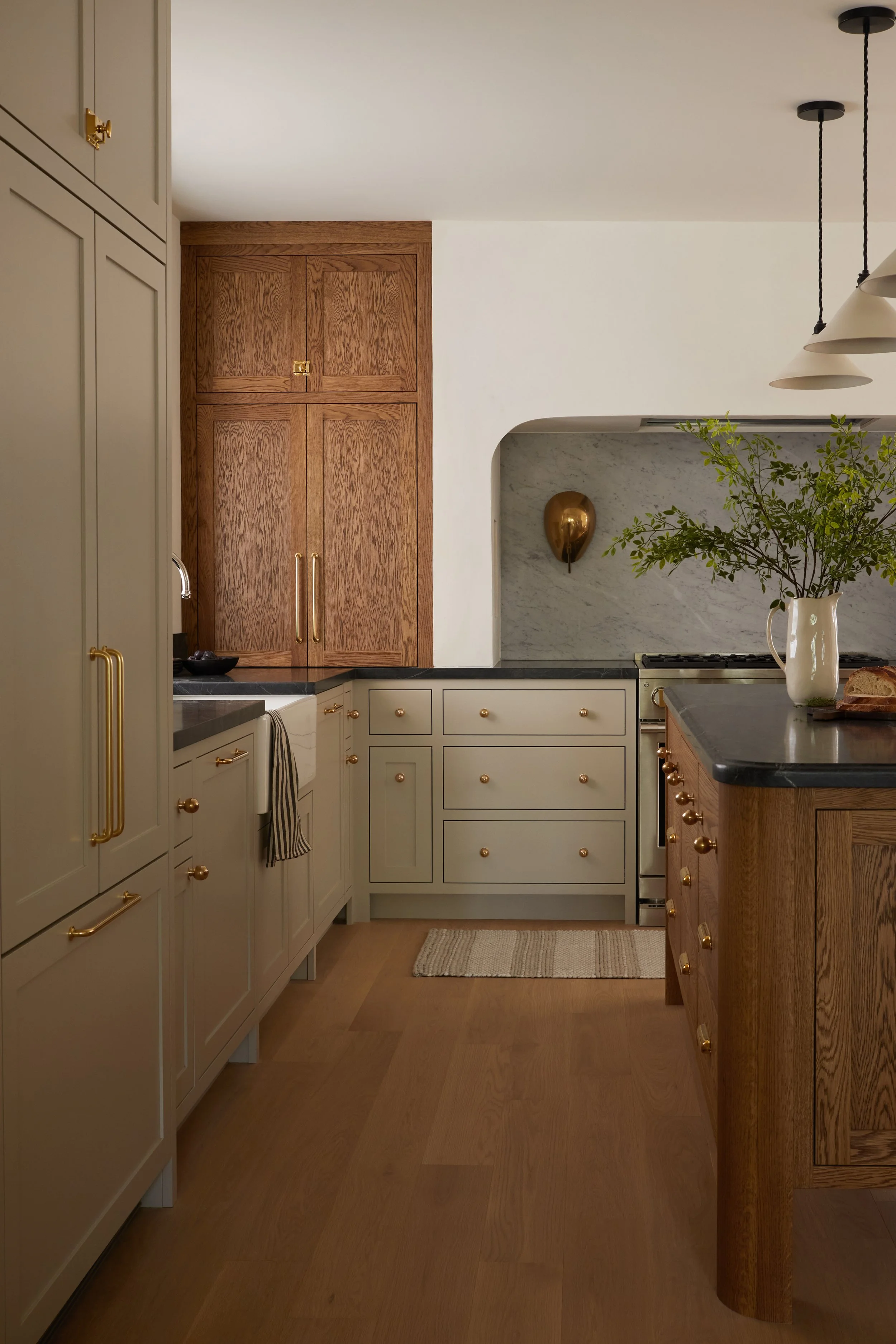 A kitchen with cream-colored cabinets, wooden accents, a marble backsplash, and a small island with a plant in a white pitcher.