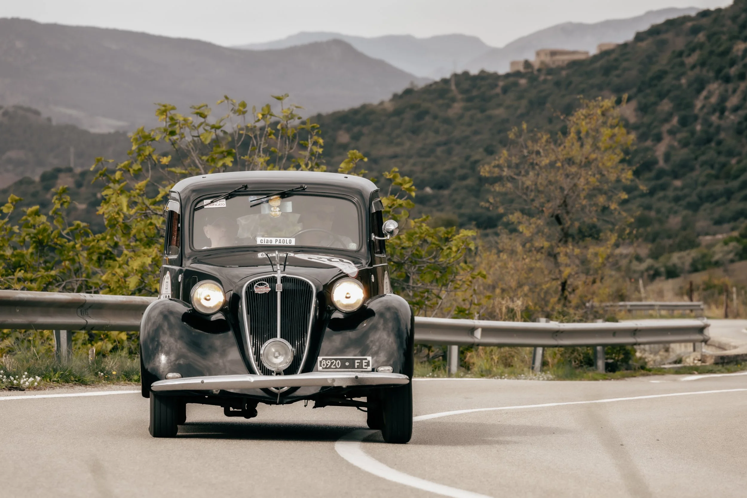Auto d'epoca nera sulla strada di montagna, con paesaggi di montagne e vegetazione in secondo piano.