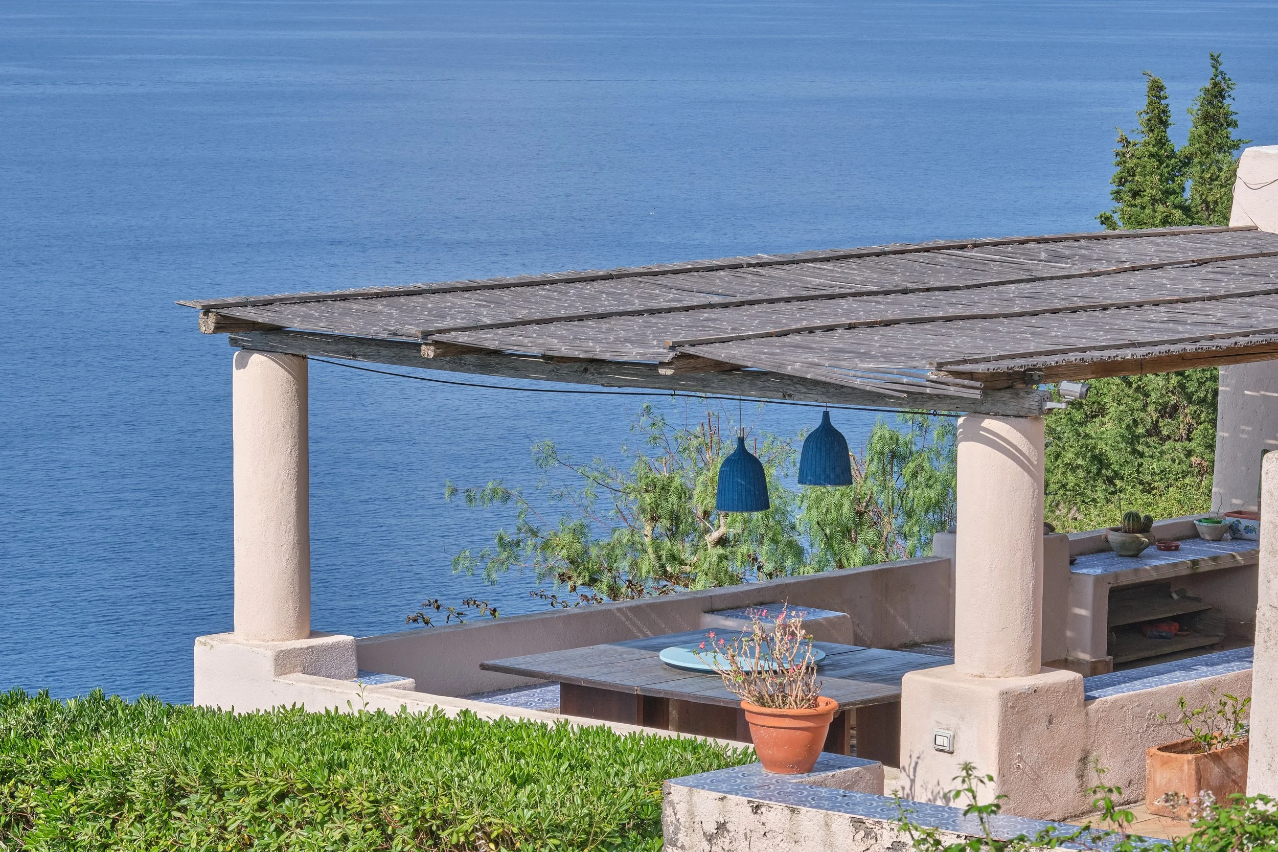 Balcone con tetto in legno che guarda su un grande lago blu, con piante verdi e decorazioni blu appese.