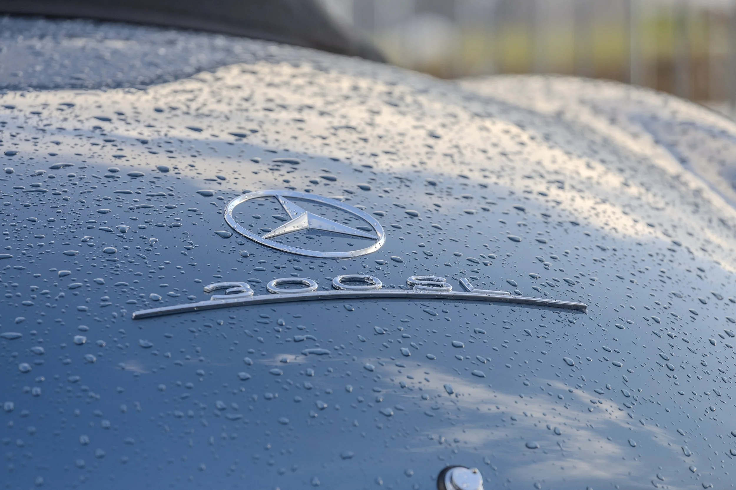 Superficie di un'auto Mercedes con gocce d'acqua sulla carrozzeria e il logo Mercedes al centro.