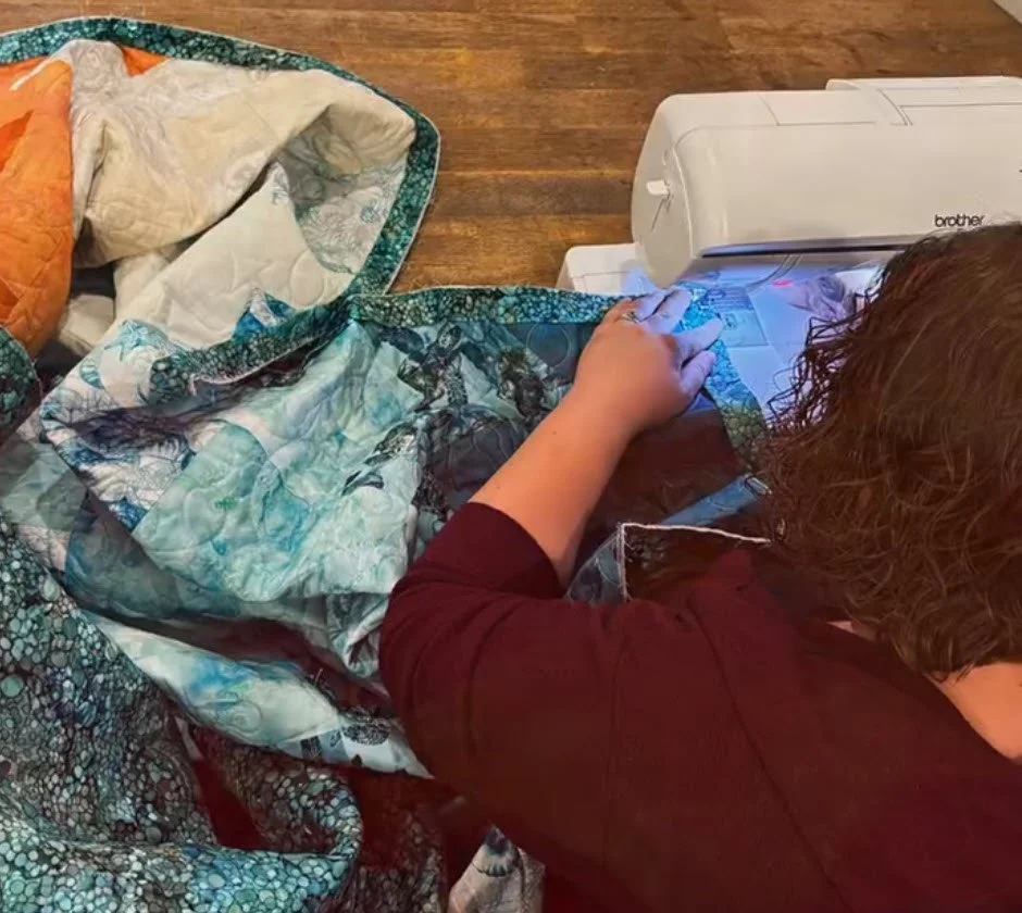 A woman using a sewing machine to quilt a fabric piece on a wooden table.