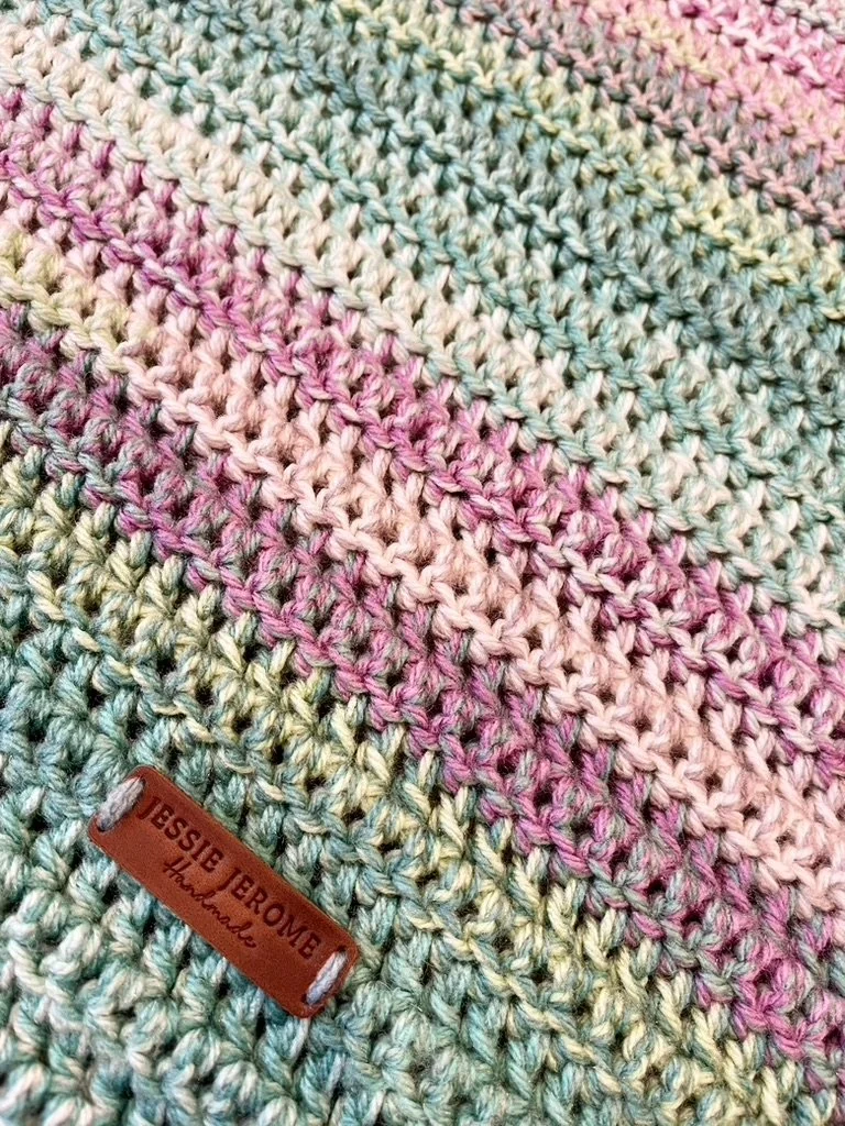 Close-up of a multicolored crocheted blanket with a leather tag that reads 'JESSIE JEROME handmade'.
